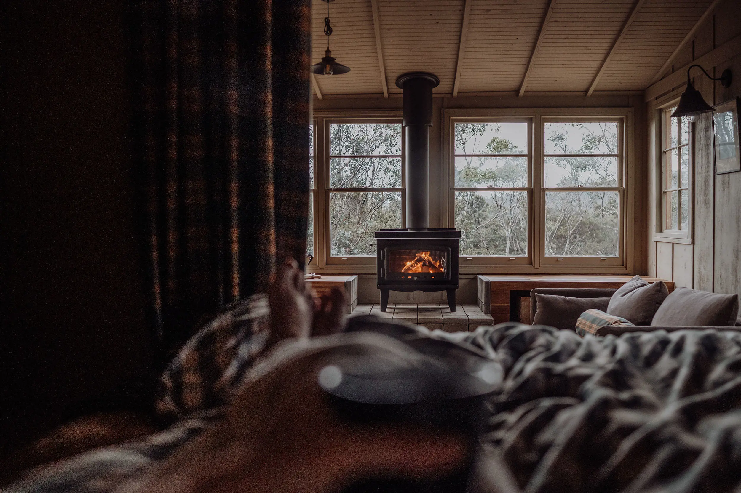 A person is lying back relaxing on a bed. From their view, we see the interior of a wooden cabin, with a roaring fireplace.