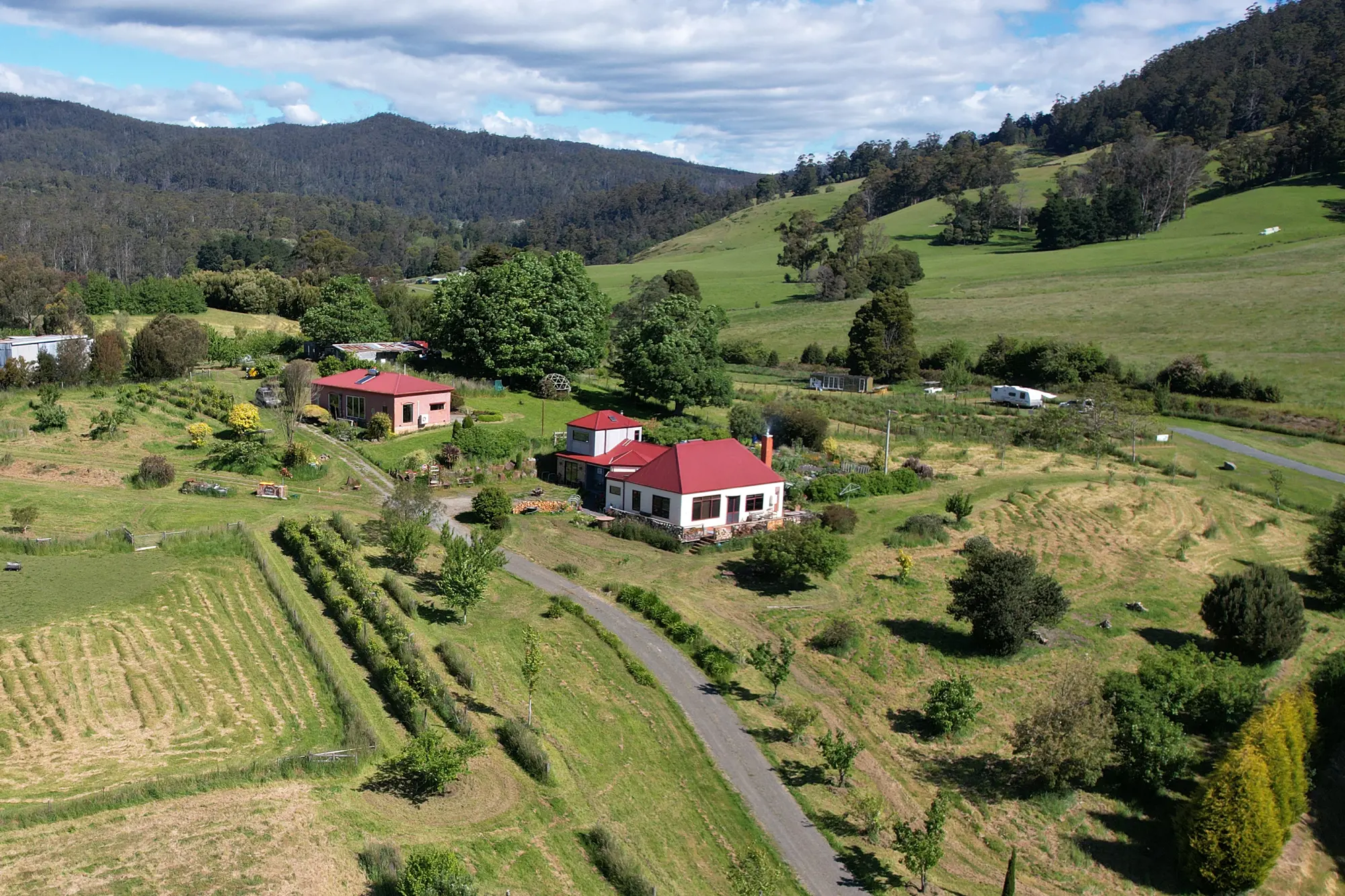 A red-roofed cottage stands amongst trees in a green valley.
