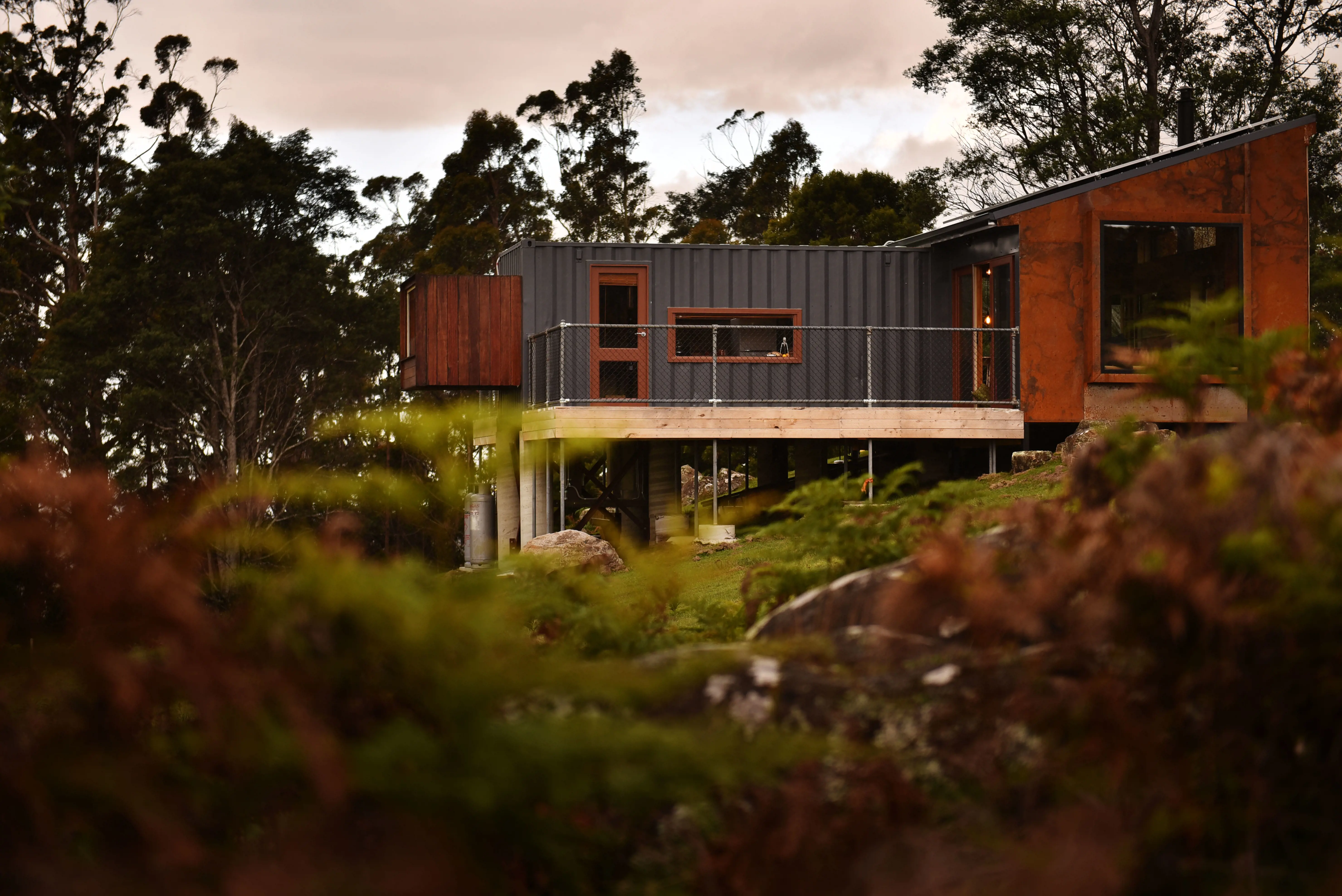 Exterior shot of the trig taken from afar among some ferns, the structure blends in with its surroundings with its natural earthy colours..