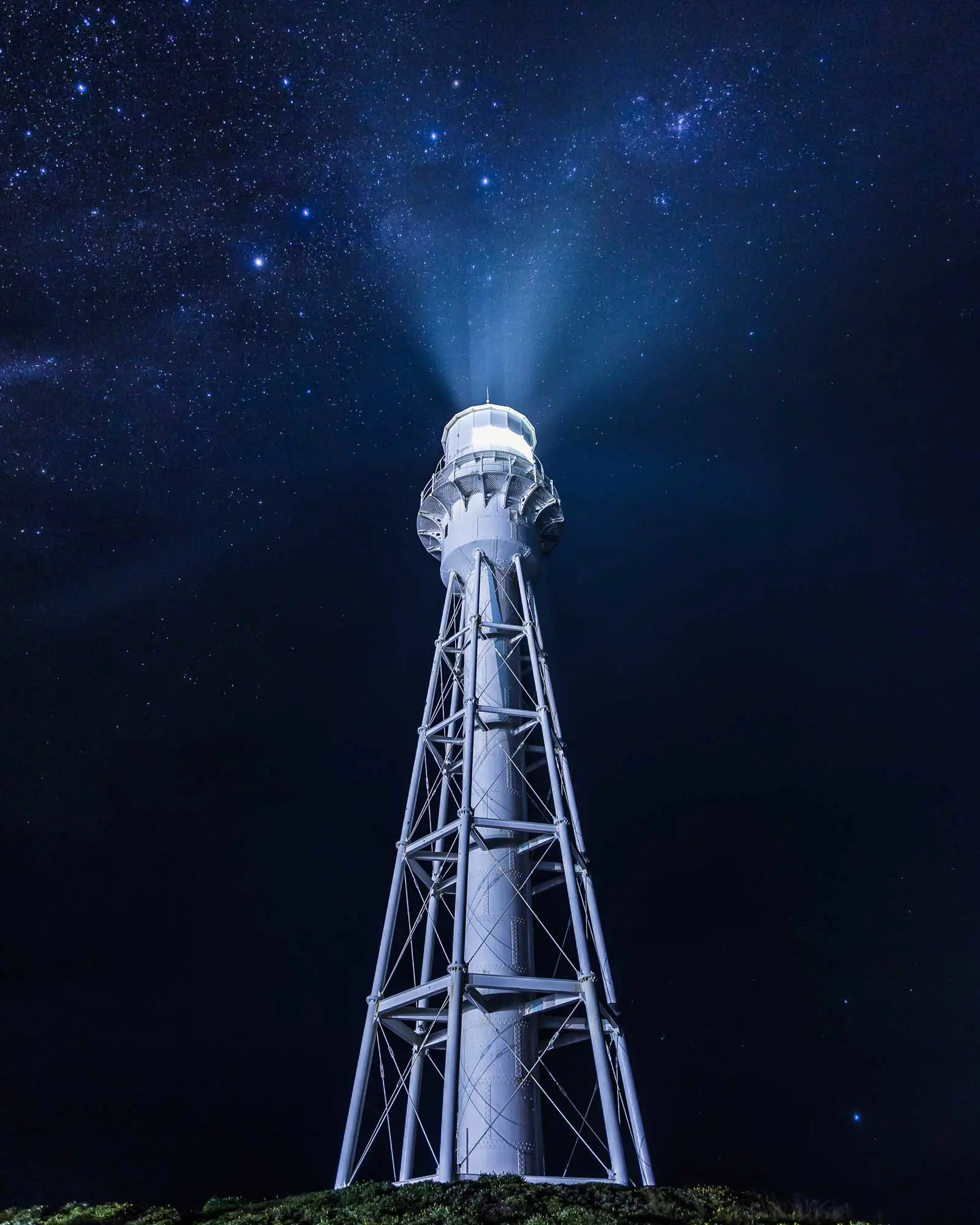 A tall white lighthouse stands against the dark, starry skies.