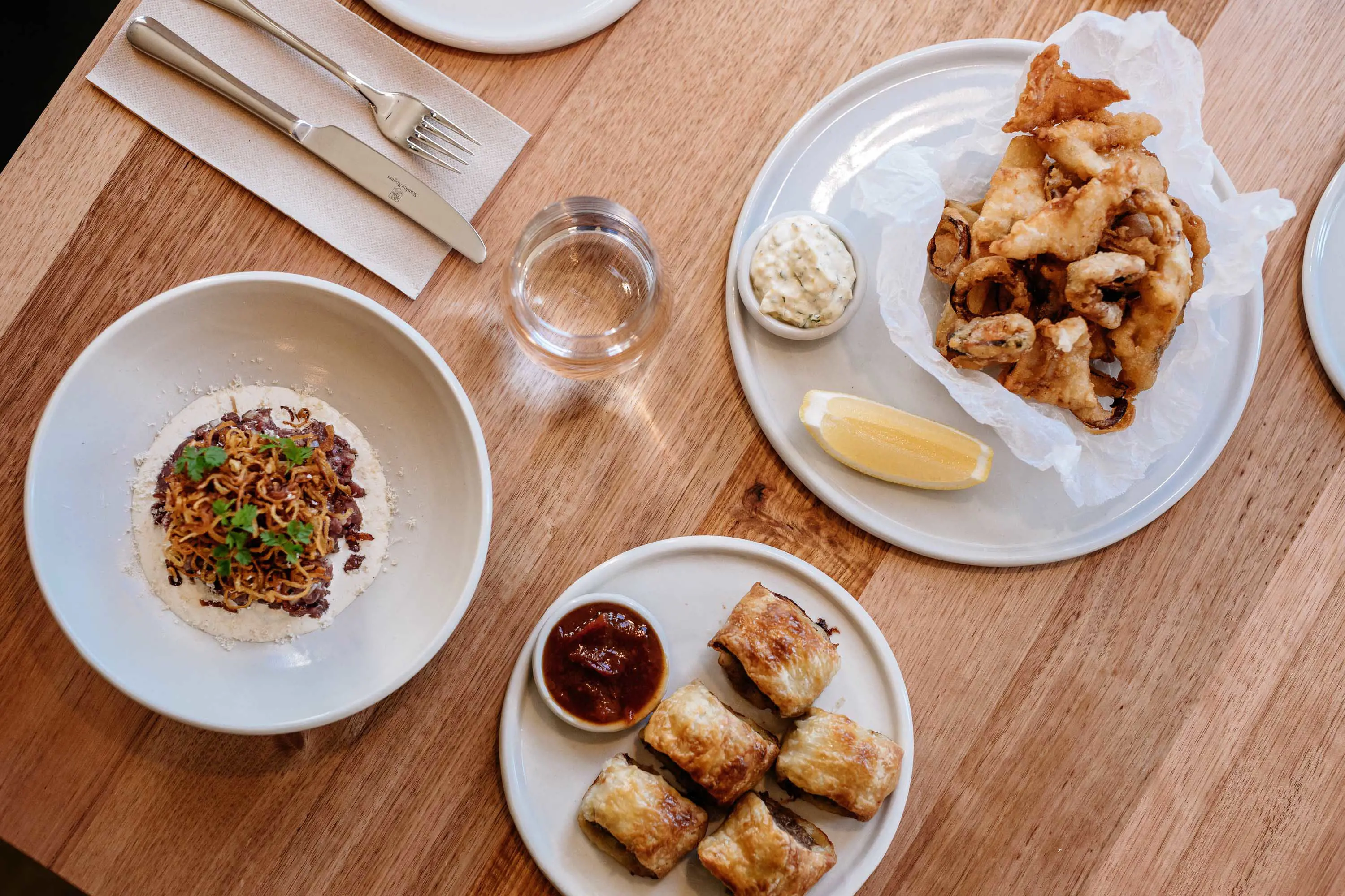 Some seafood, pastries and a noodle dish on white plates sitting on a wooden table.