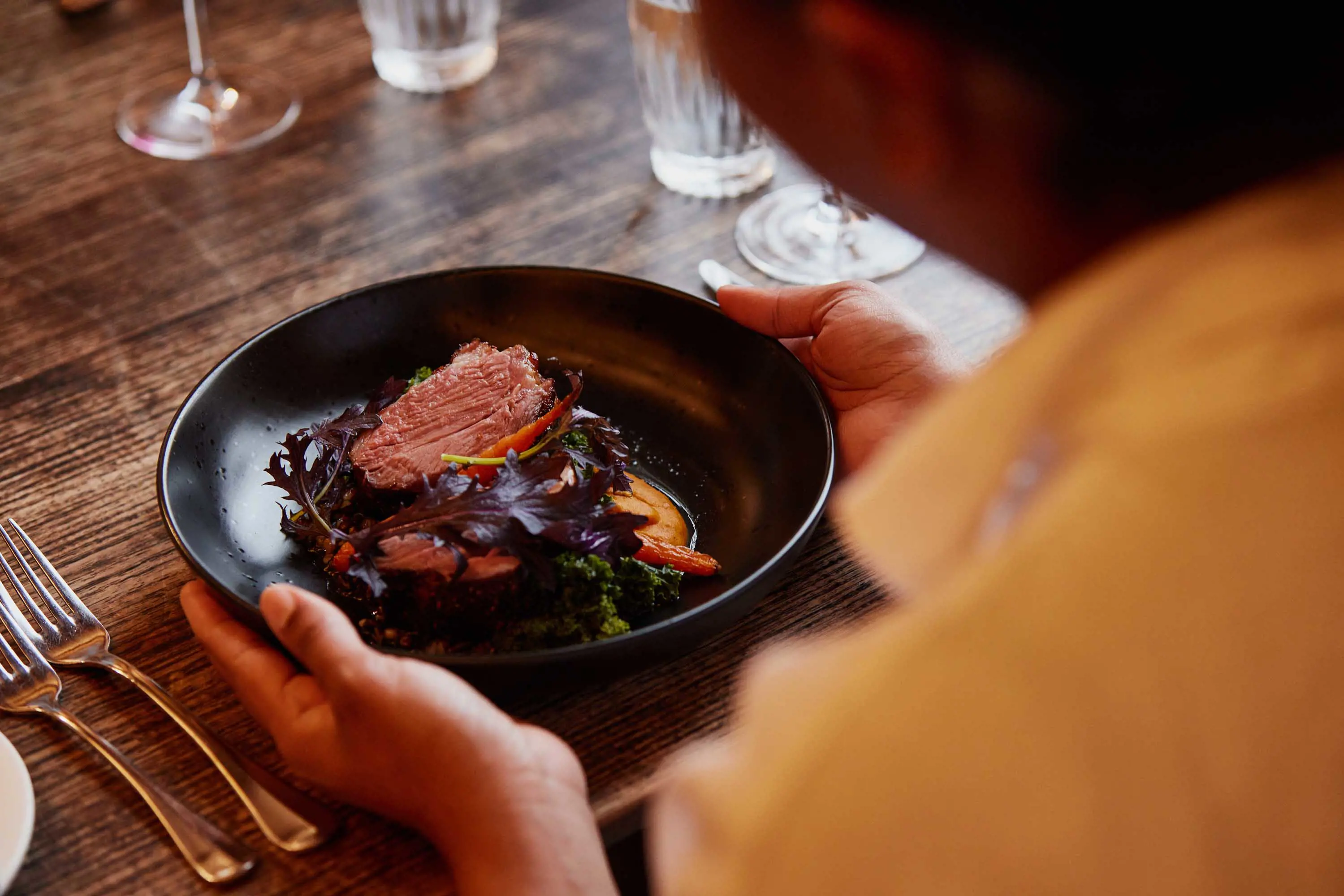 A small, black dish with a slice of beef placed on top of vegetables.