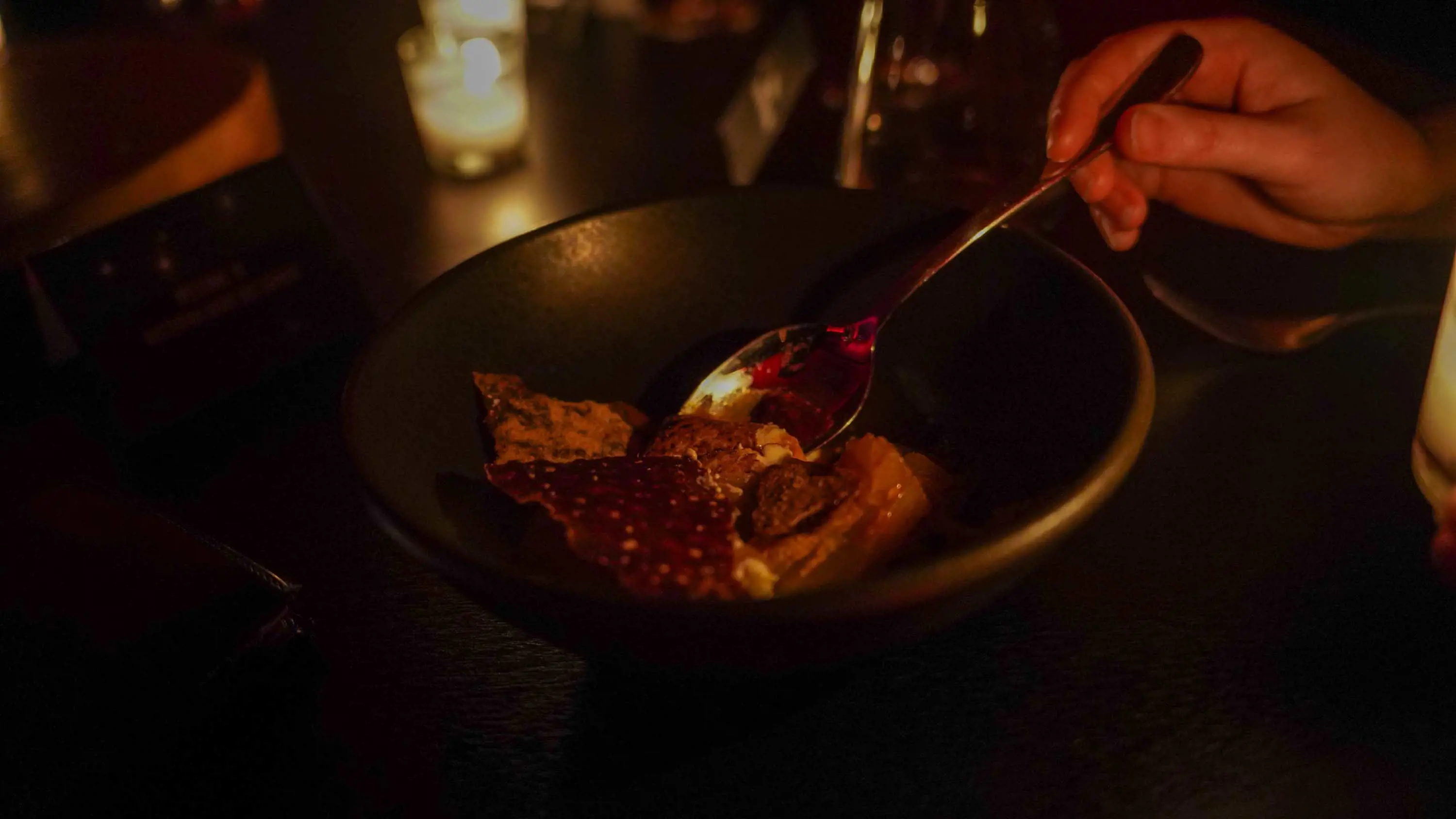 A dish with roasted vegetables sits on a table lit by candlelight.