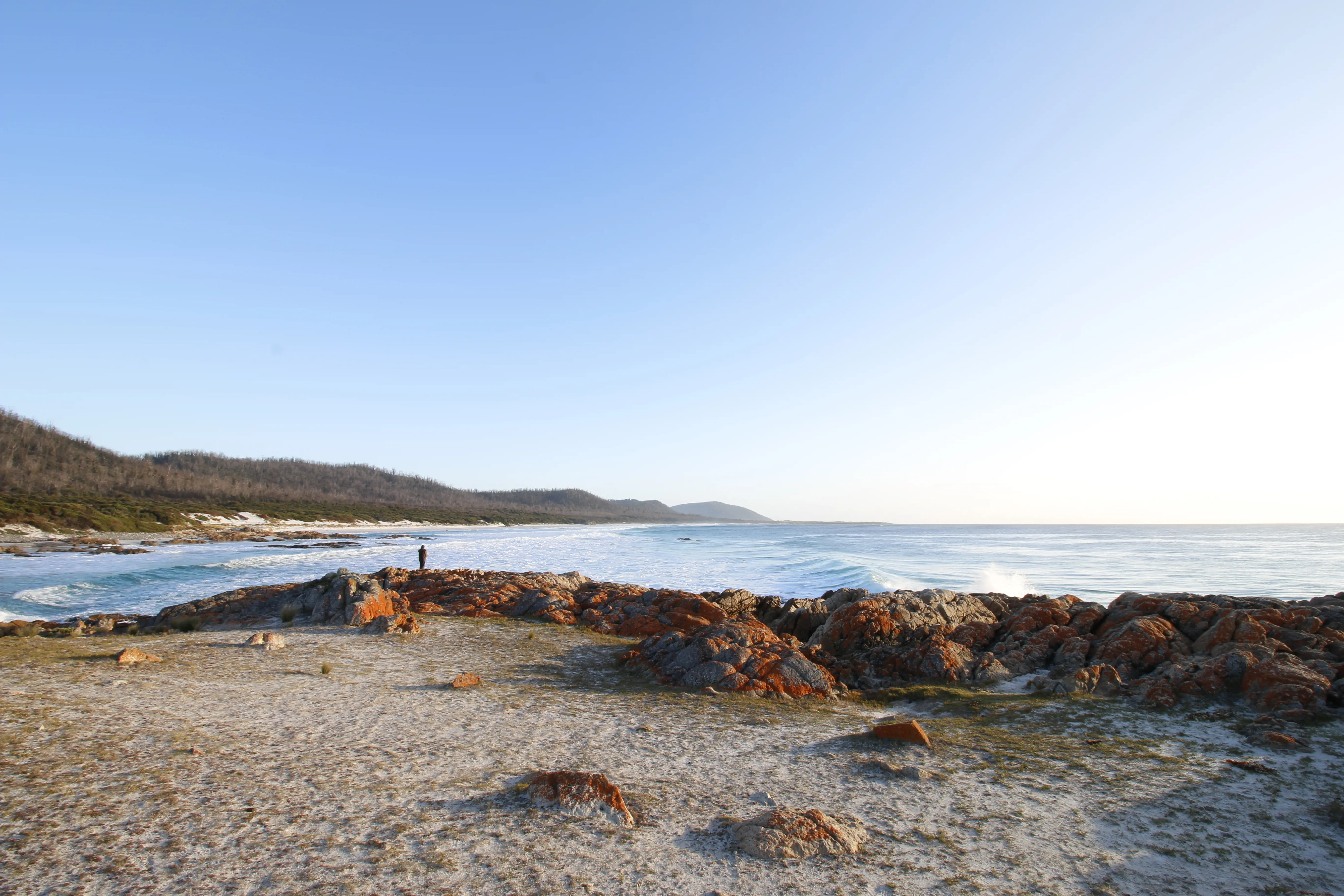 Person standing on a rocky outcrop looking across Friendly Beaches at Freycinet National Park