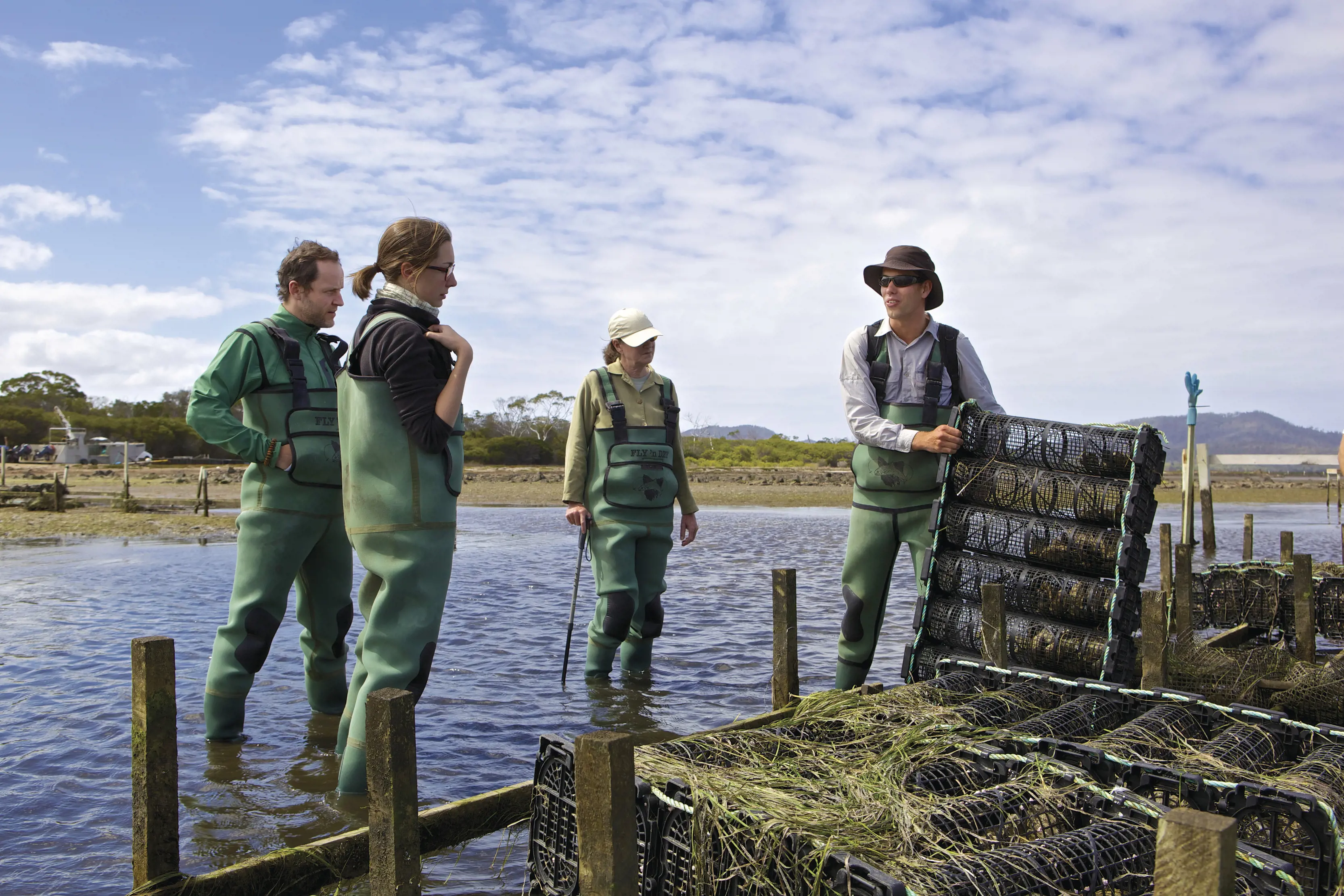Tour guide and three tourists geared up, in the water, learning about the Freycinet Marine Farm.