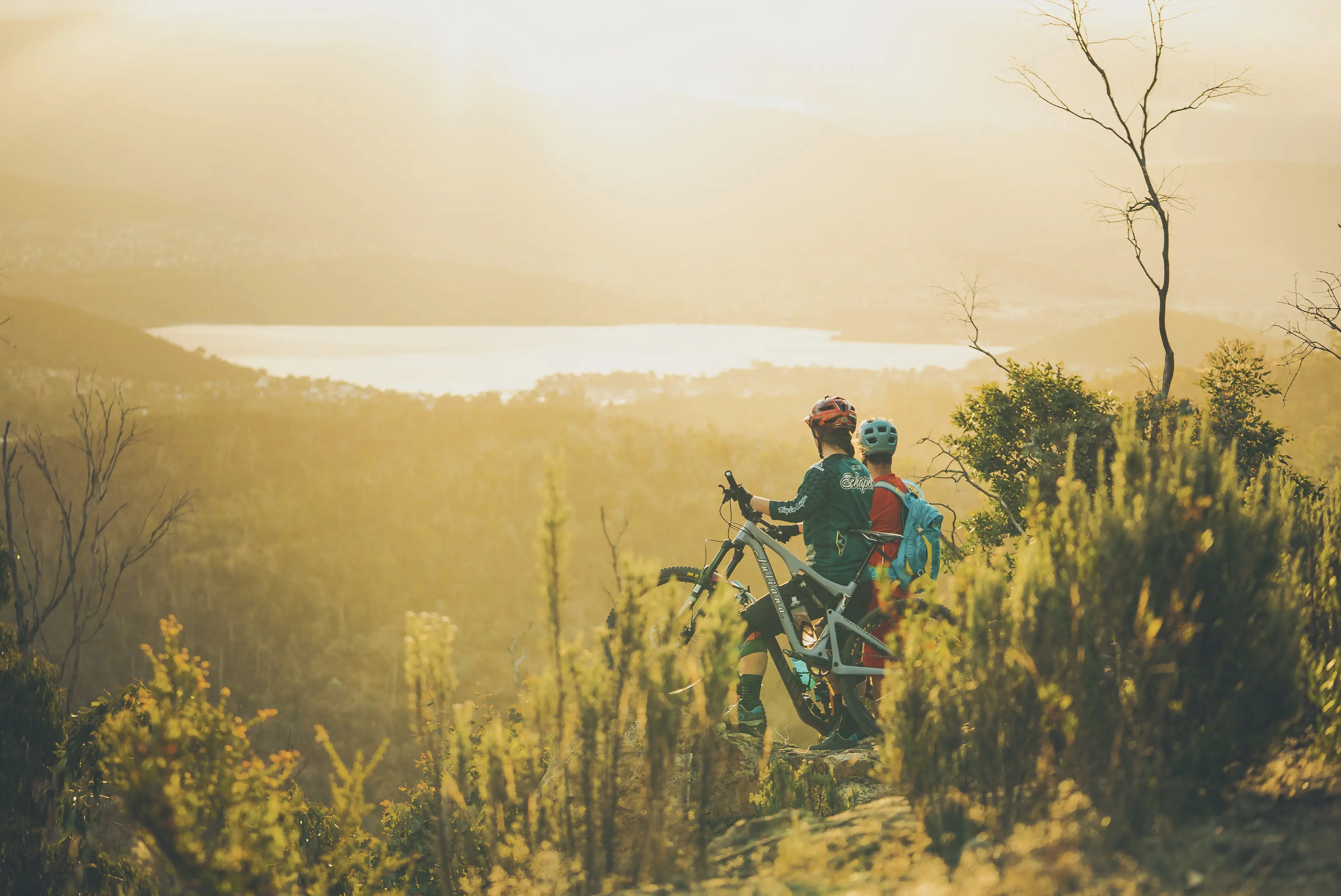 From behind greenery, cyclists stop and look out on the The Clarence Mountain Bike Park clifftop track, in the Meehan Range.