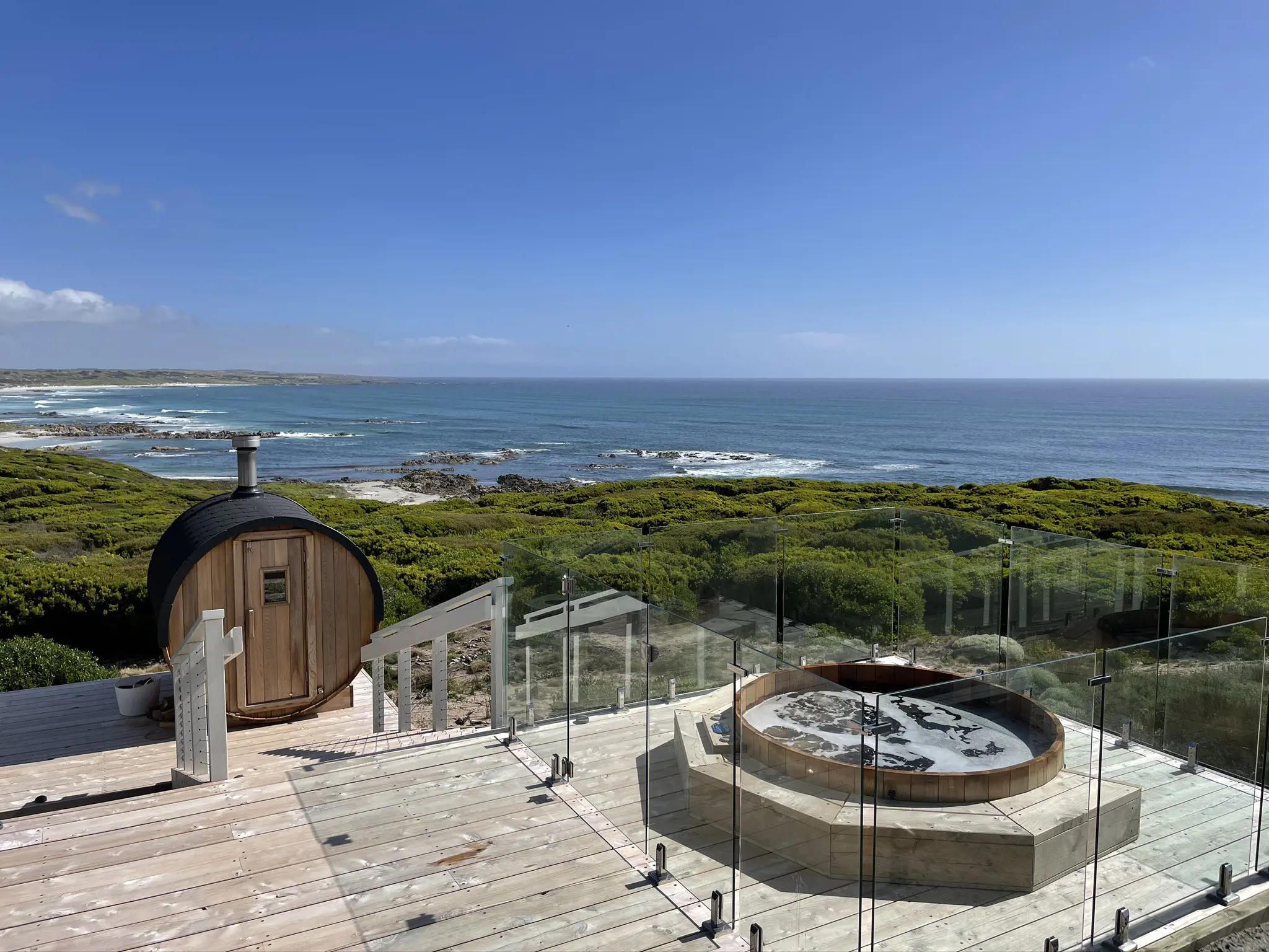 Exterior of the wrap around outdoor deck featuring an outdoor hot tub spa and red cedar sauna, both with ocean views, at Taraki Lodge.