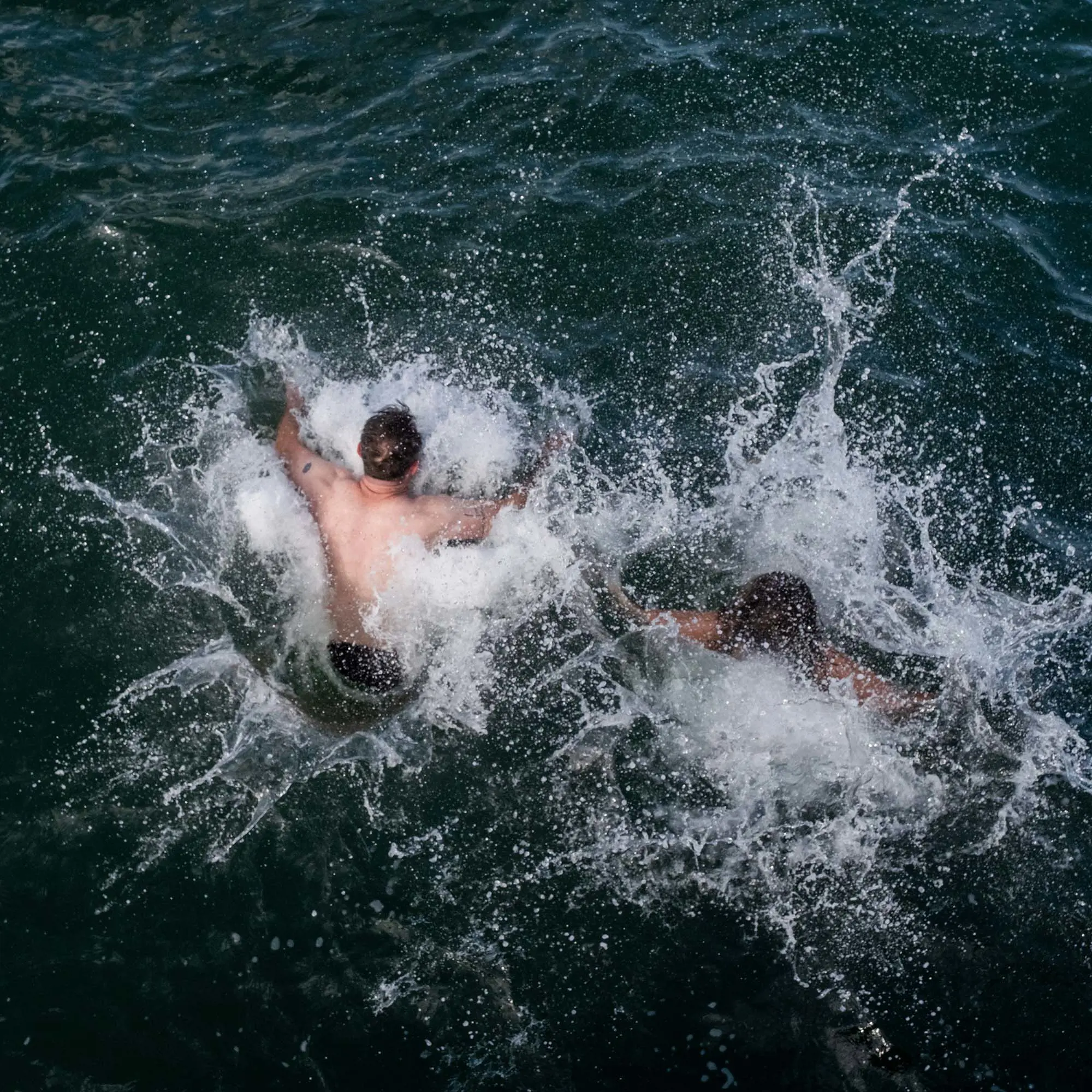 Water splashes up as two people land in the lake after jumping in.