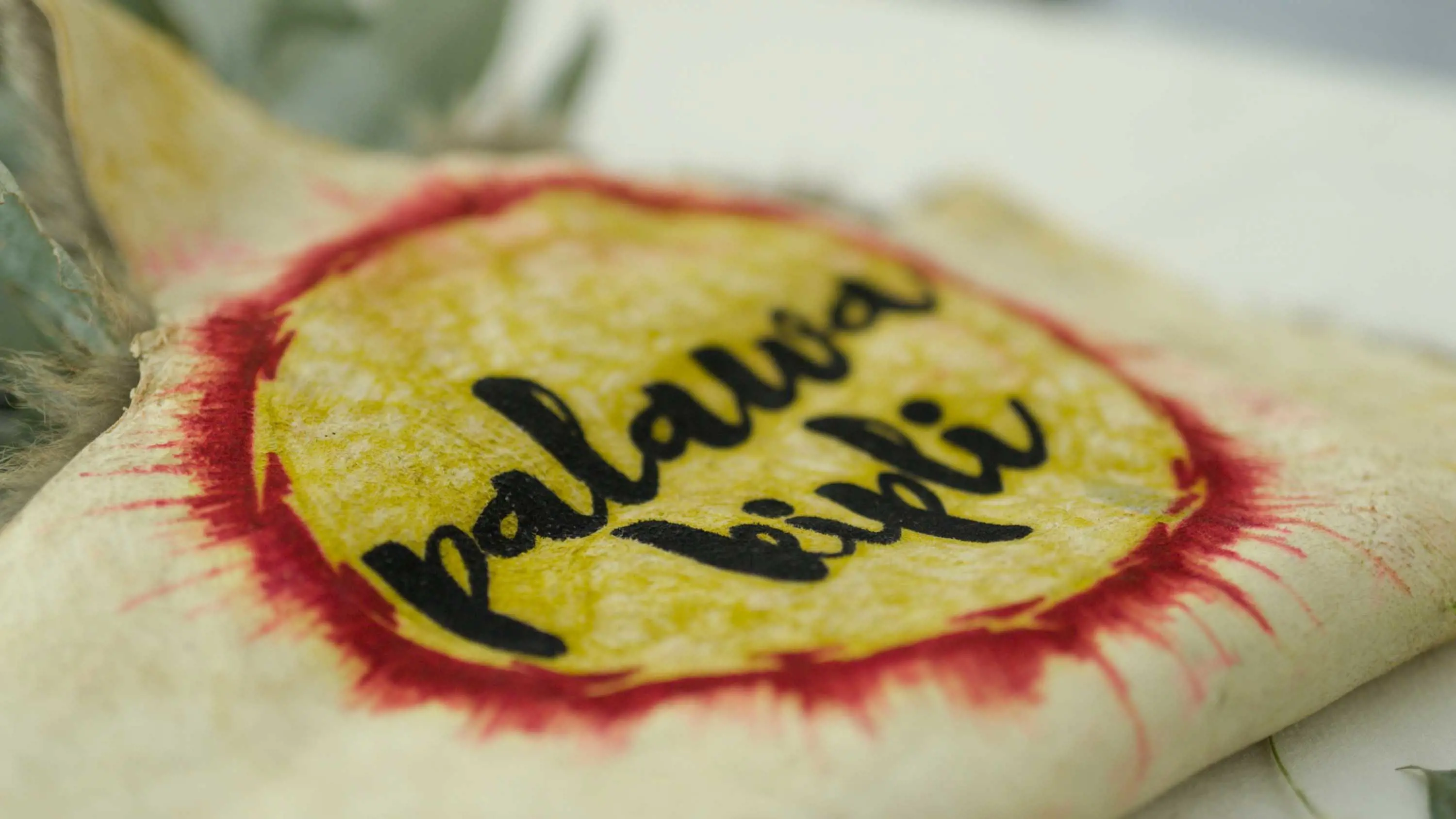 A yellow and red logo with black cursive writing that reads palawa kipli.