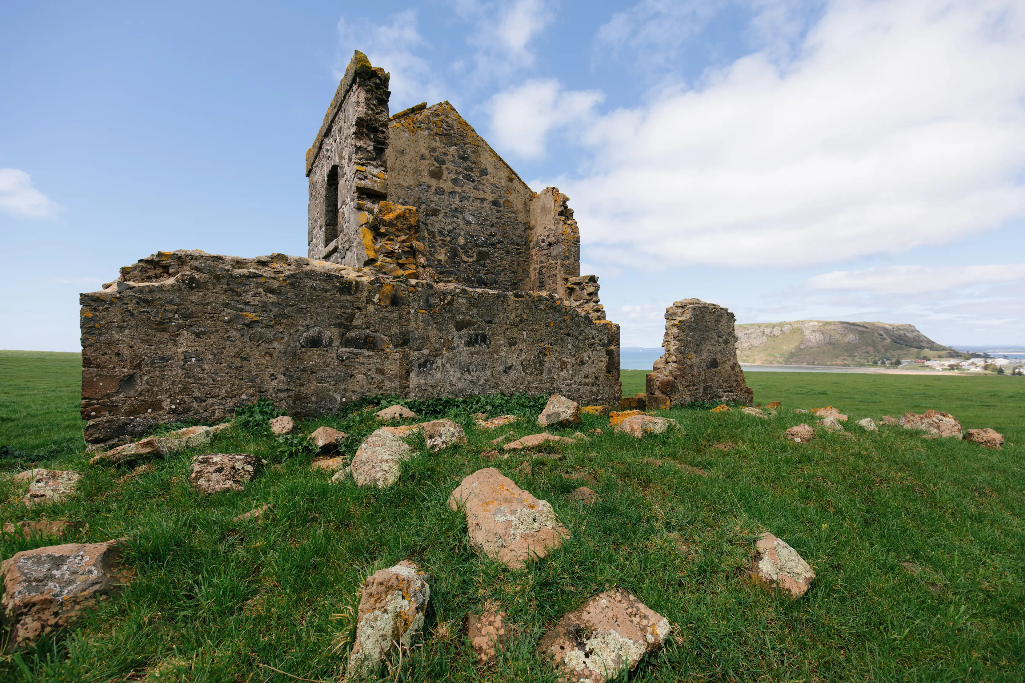 Exterior of the remains of a building at Highfield Historic Site, with The Nut in the distance in the background.