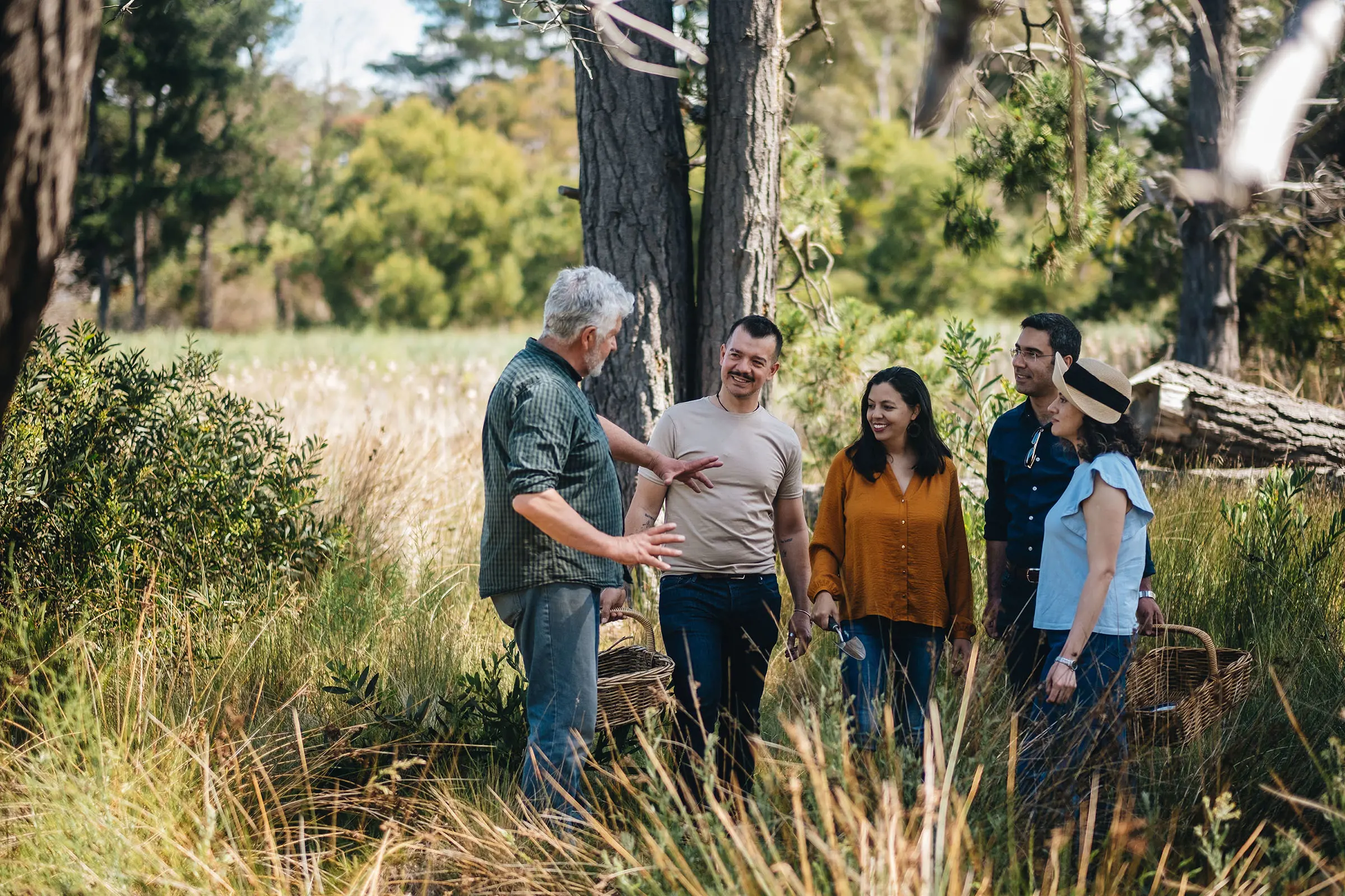 A man gestures as he speaks to four tour guests, standing amongst the bush.