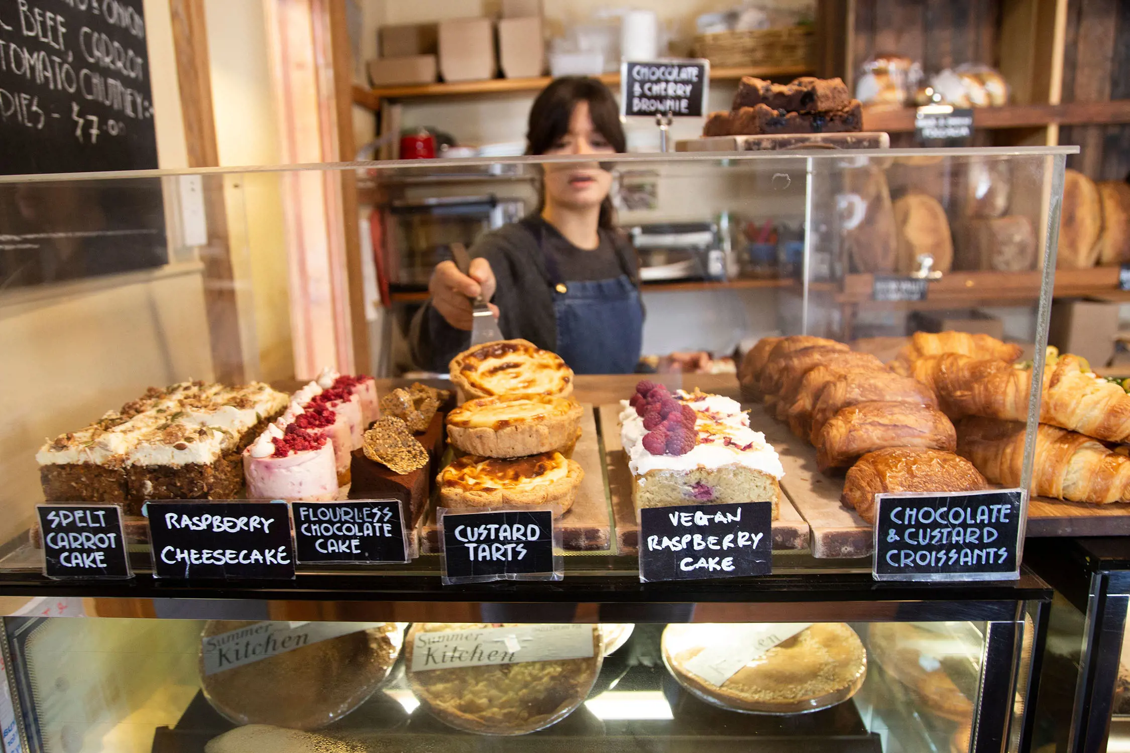 A bakery sweets cabinet, fully stocked with rows of goods including carrot cake slices, mini cheesecakes, custard tarts and croissants.