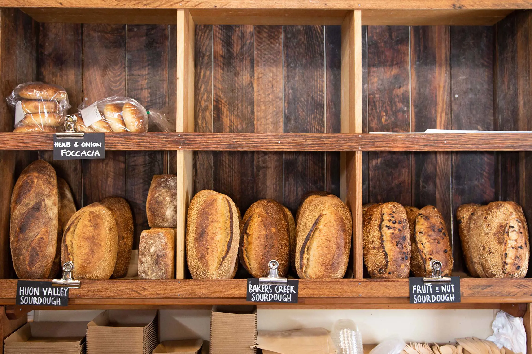 Wooden pigeon-hole shelves mounted on the wall, each filled with crusty loaves of bread of all different styles and sizes.