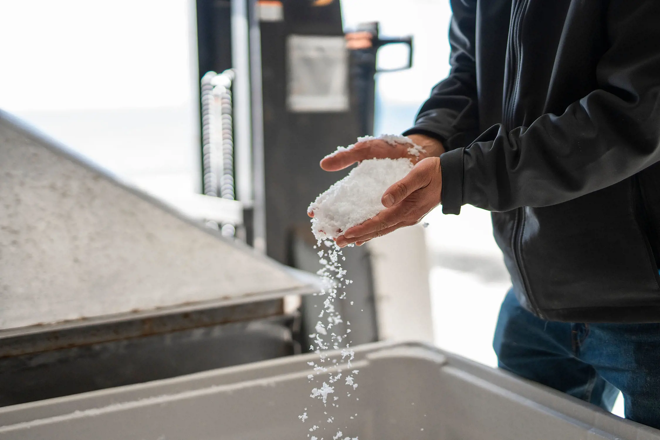 A person leans over a large silver trough, holding a huge pile of salt in their hands.