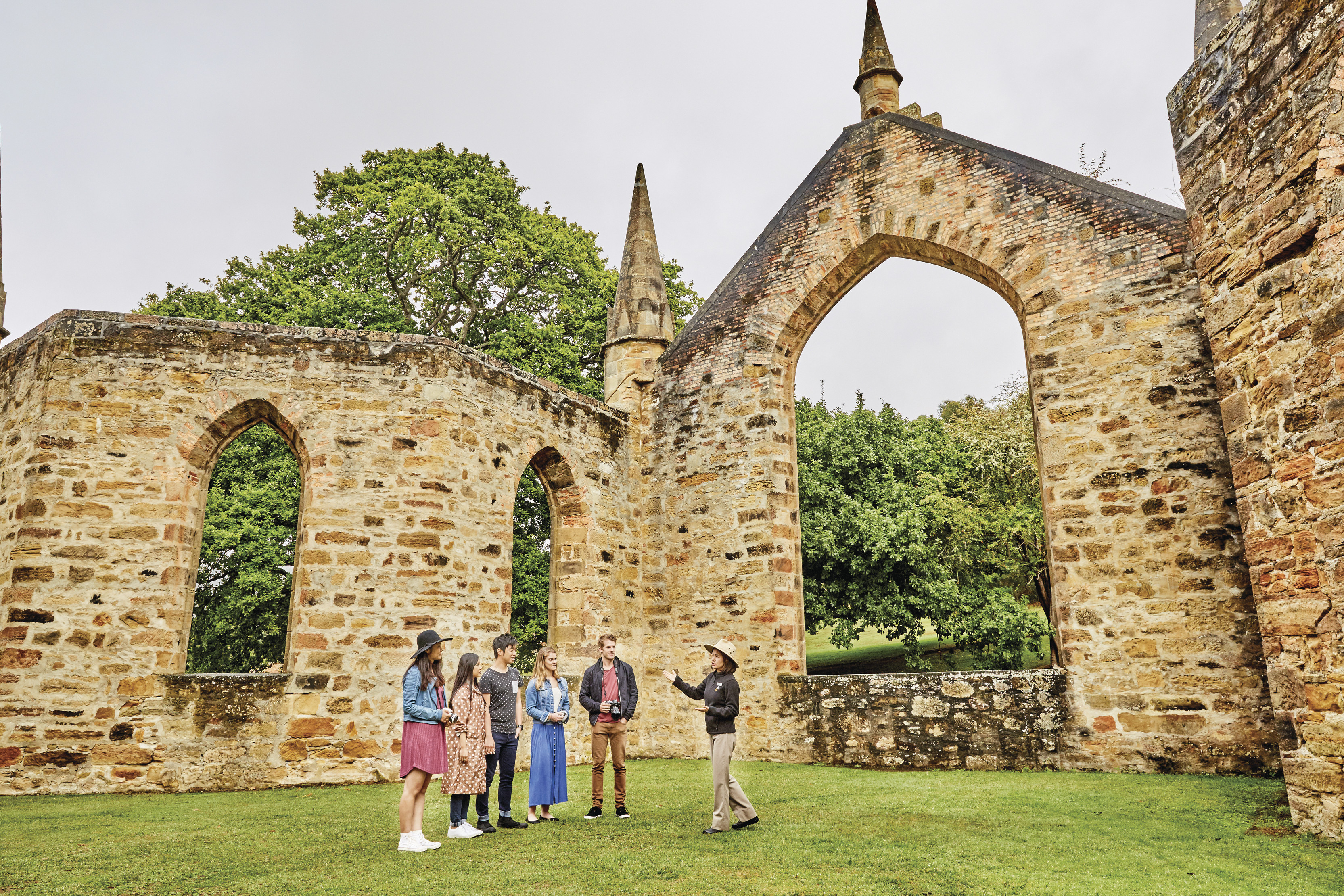 Tour guide talking to the tourists about the Port Arthur Historic Site. Old stone walls surround them.