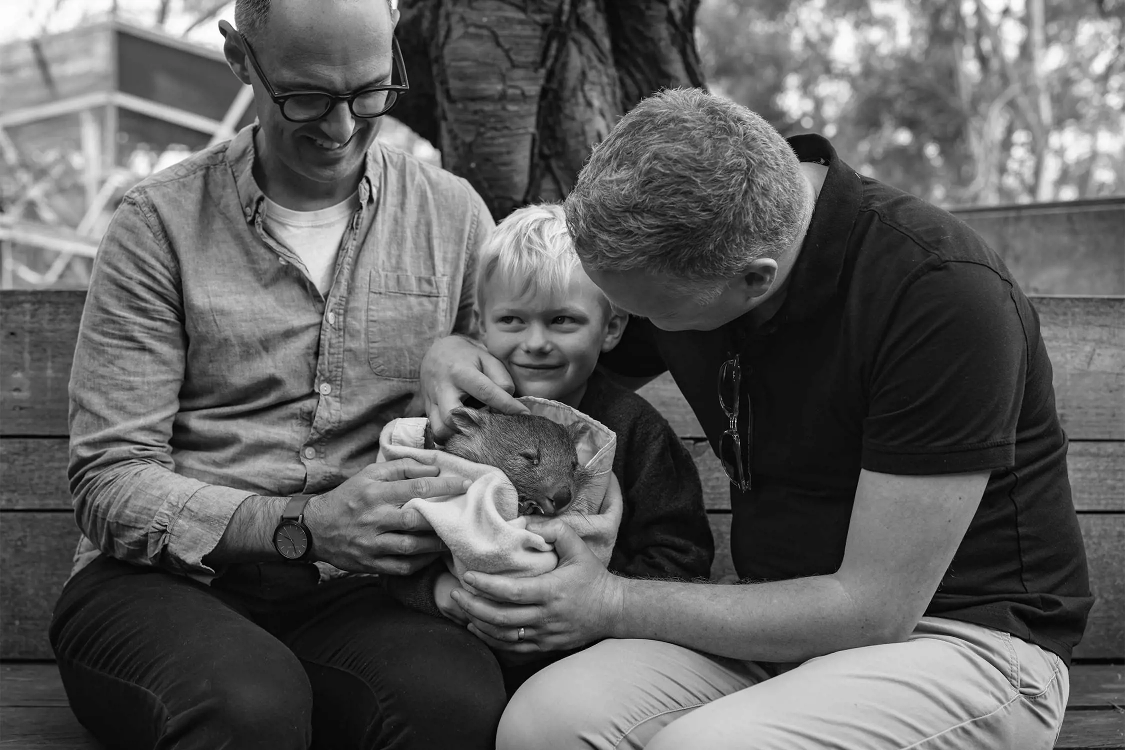 Two adults and a child are smiling while holding a tawny frogmouth bird wrapped in a blanket.