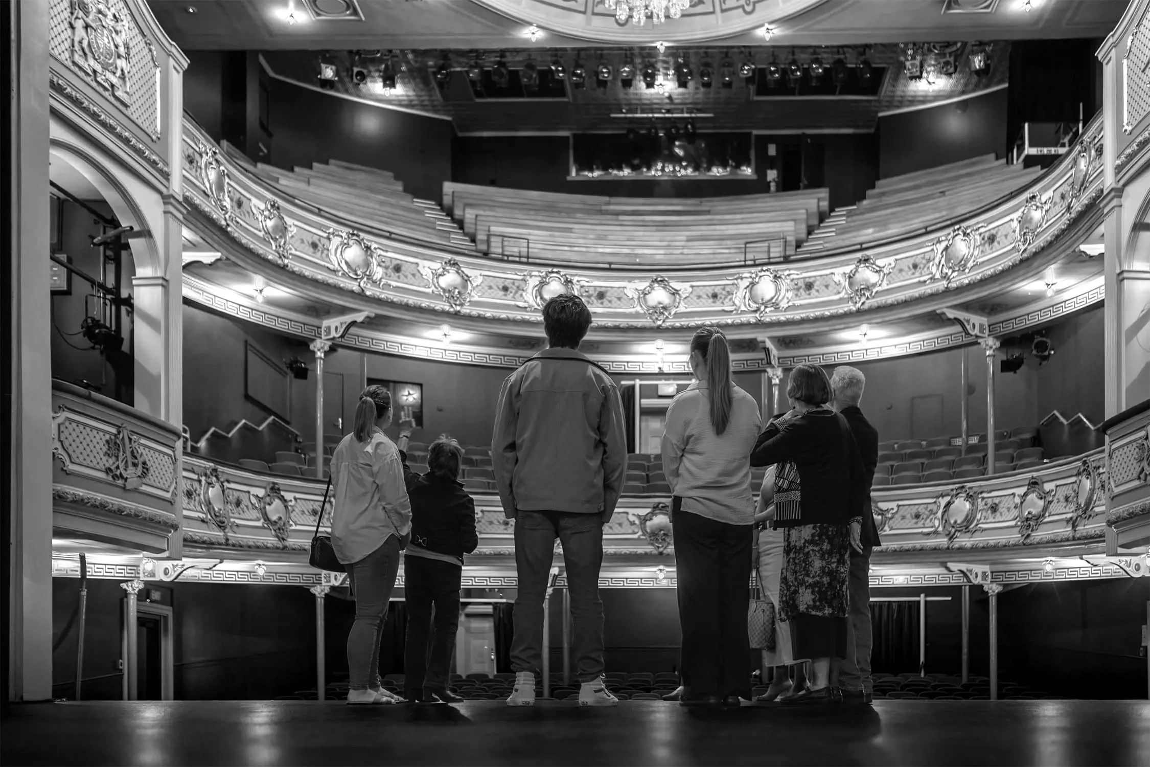 A group of seven people observe a beautiful theatre interior from the stage area.