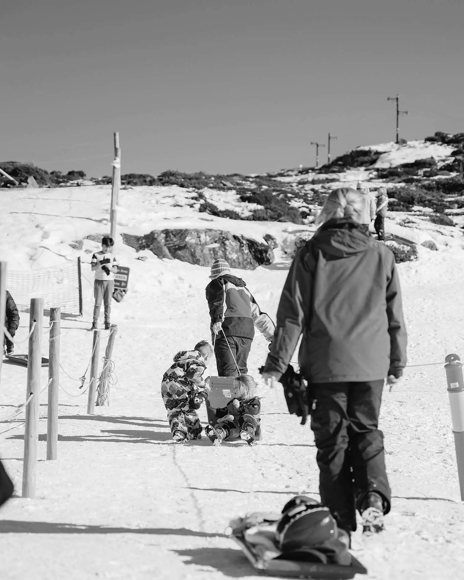 People in winter attire pull sleds across a snowy landscape, while others play in the background.