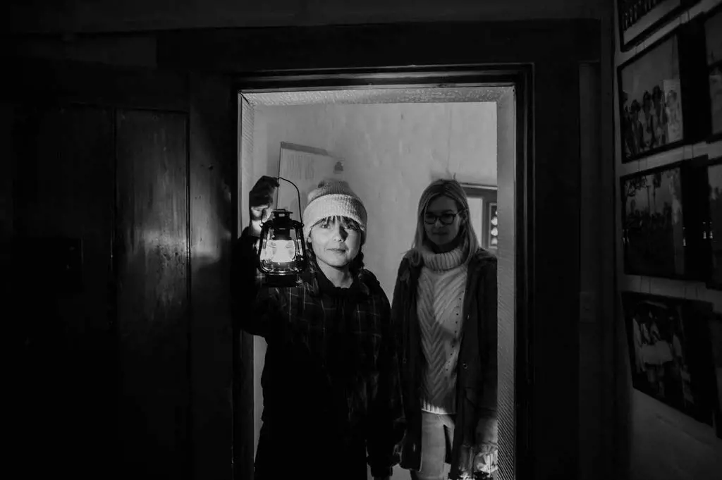 A person holding a lantern stands in a doorway, while another person stands beside them