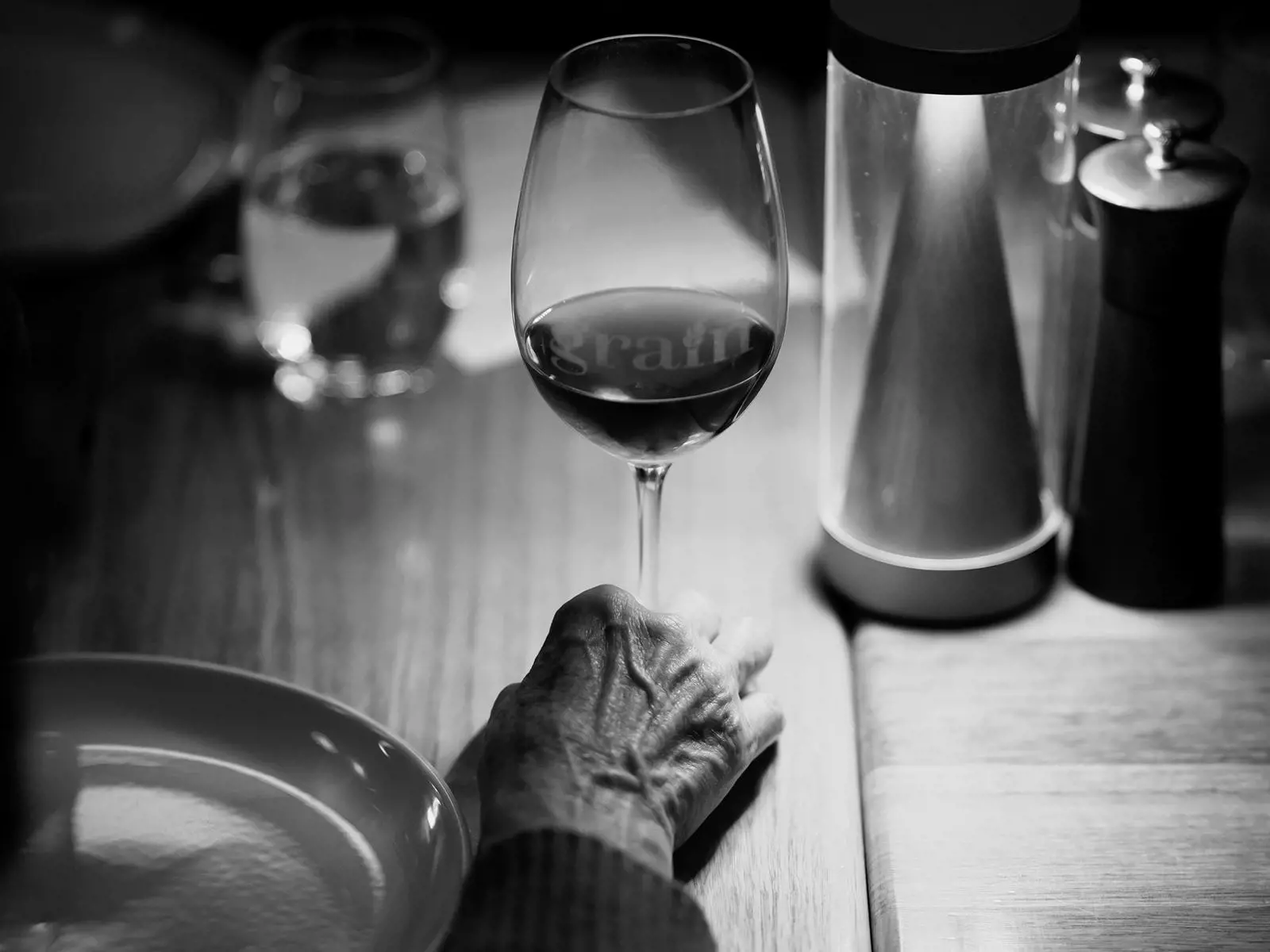 A hand rests beside a glass of red wine on a warmly lit dining table, capturing a quiet moment at Grain of the Silos.
