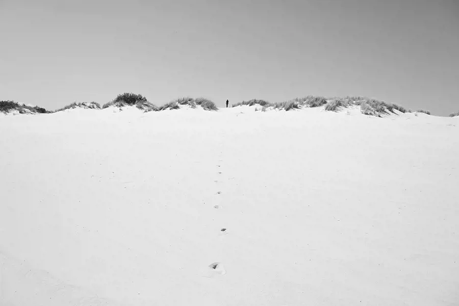 Golden sand dunes rise and fall under a moody winter sky at Henty Dunes, brushed by chilly coastal winds. Footprints disappear up into the dunes.