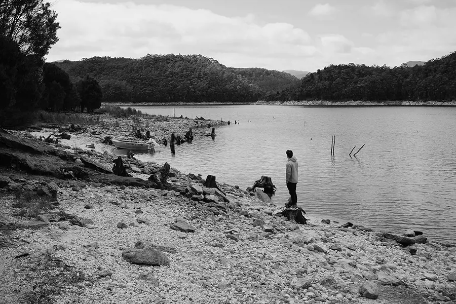 Calm waters of Lake Burbury reflect the moody, clouded sky, framed by rugged mountains under a soft winter light.