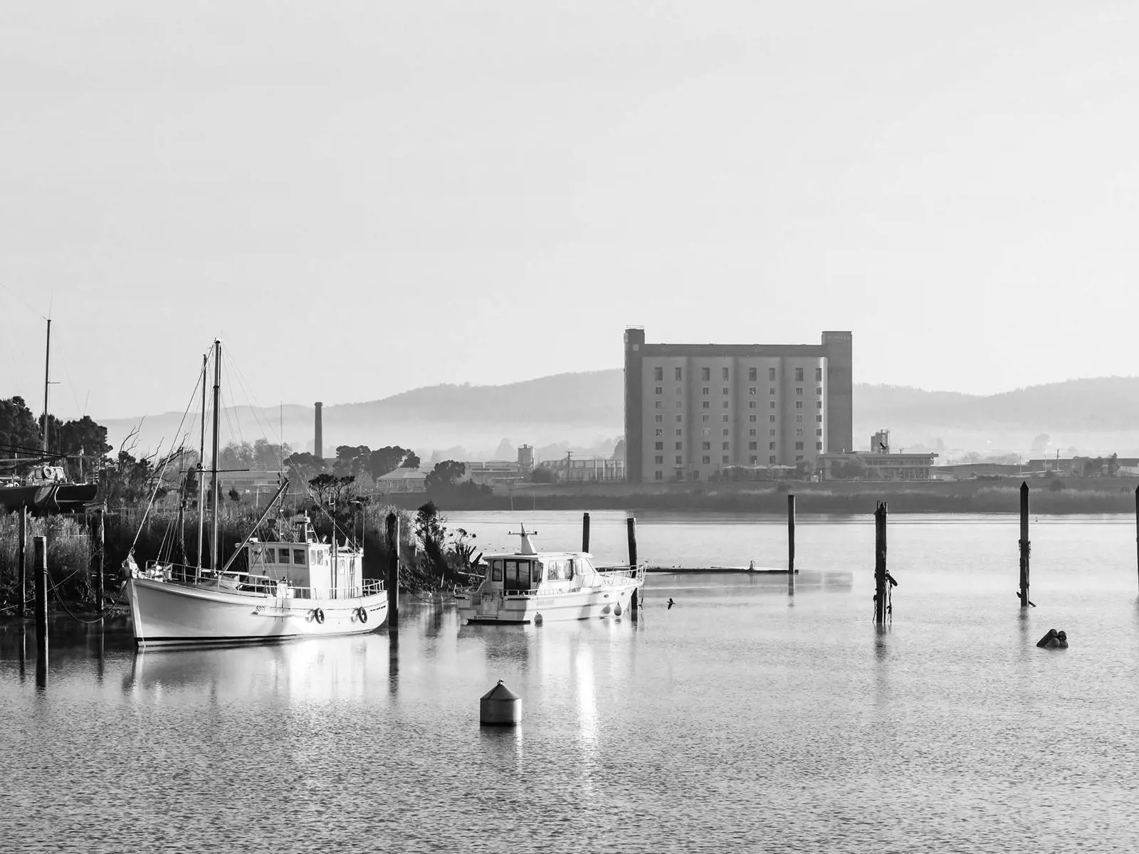 Fishing boats sit calmly on glassy water in the early morning light, with the Peppers Silo Hotel rising in the misty distance.