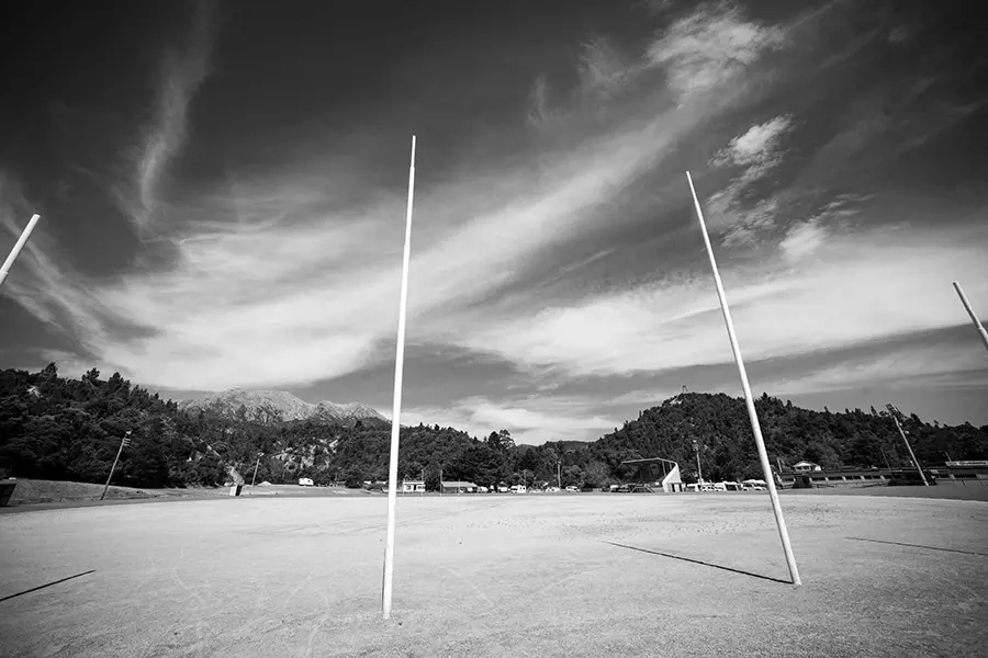 The goalposts rise up from the gravel-covered ground of a football oval surrounded by misty hills in Queenstown.