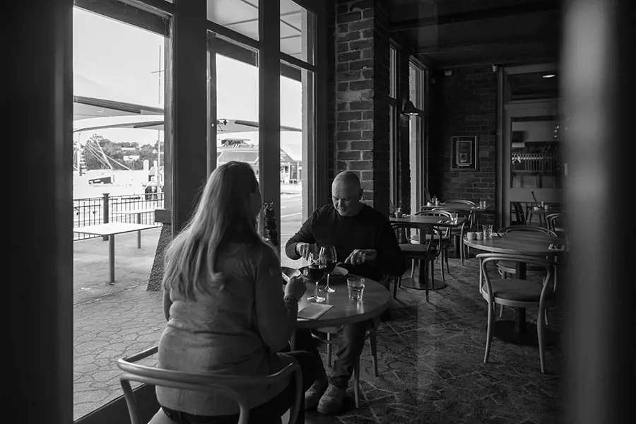 Two people sit at a small table eating a meal together by the window in a warm, inviting bar in Strahan.