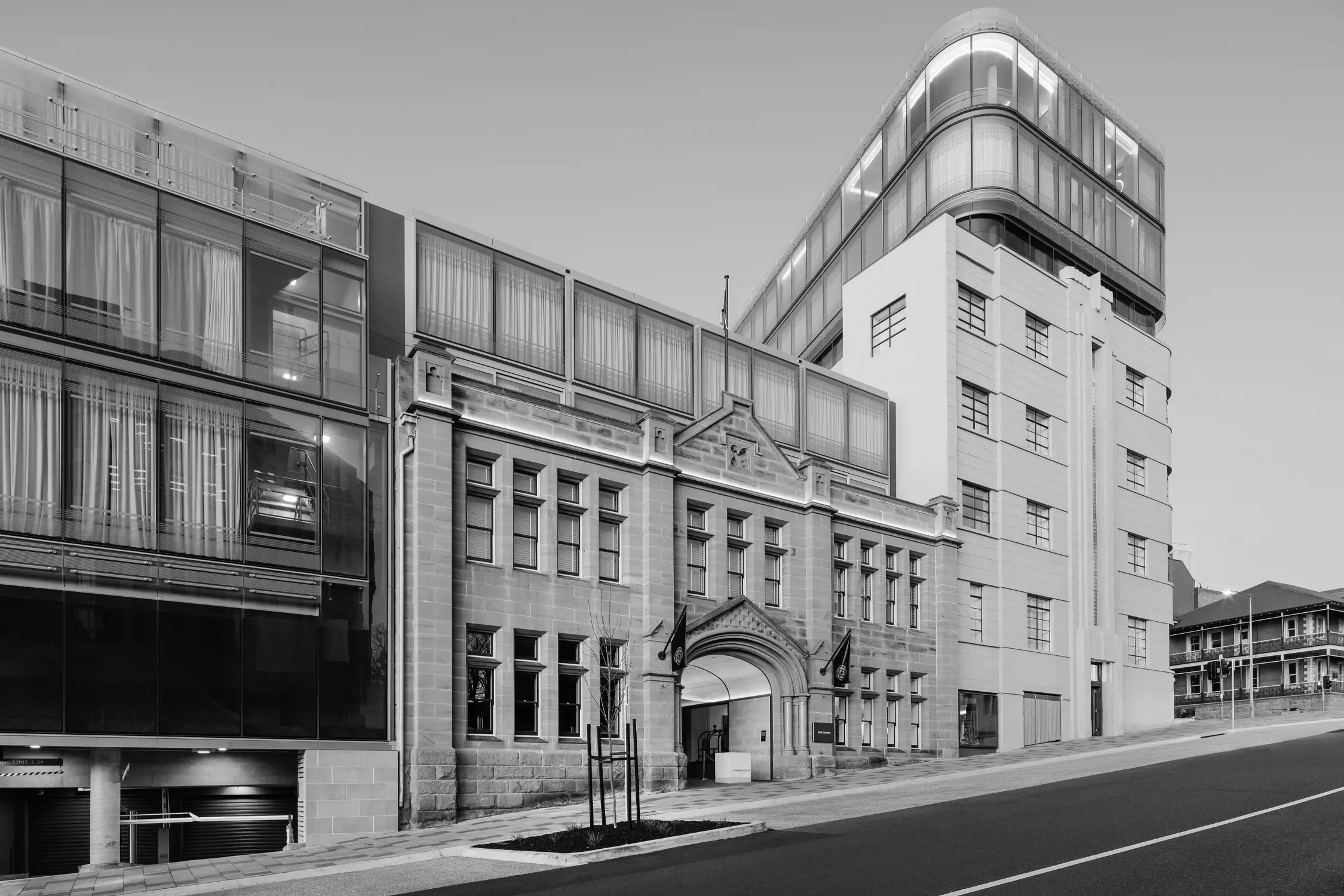 Exterior shot of a modern hotel building that blends contemporary glass design with historic stone architecture, situated on a slightly sloped urban street.