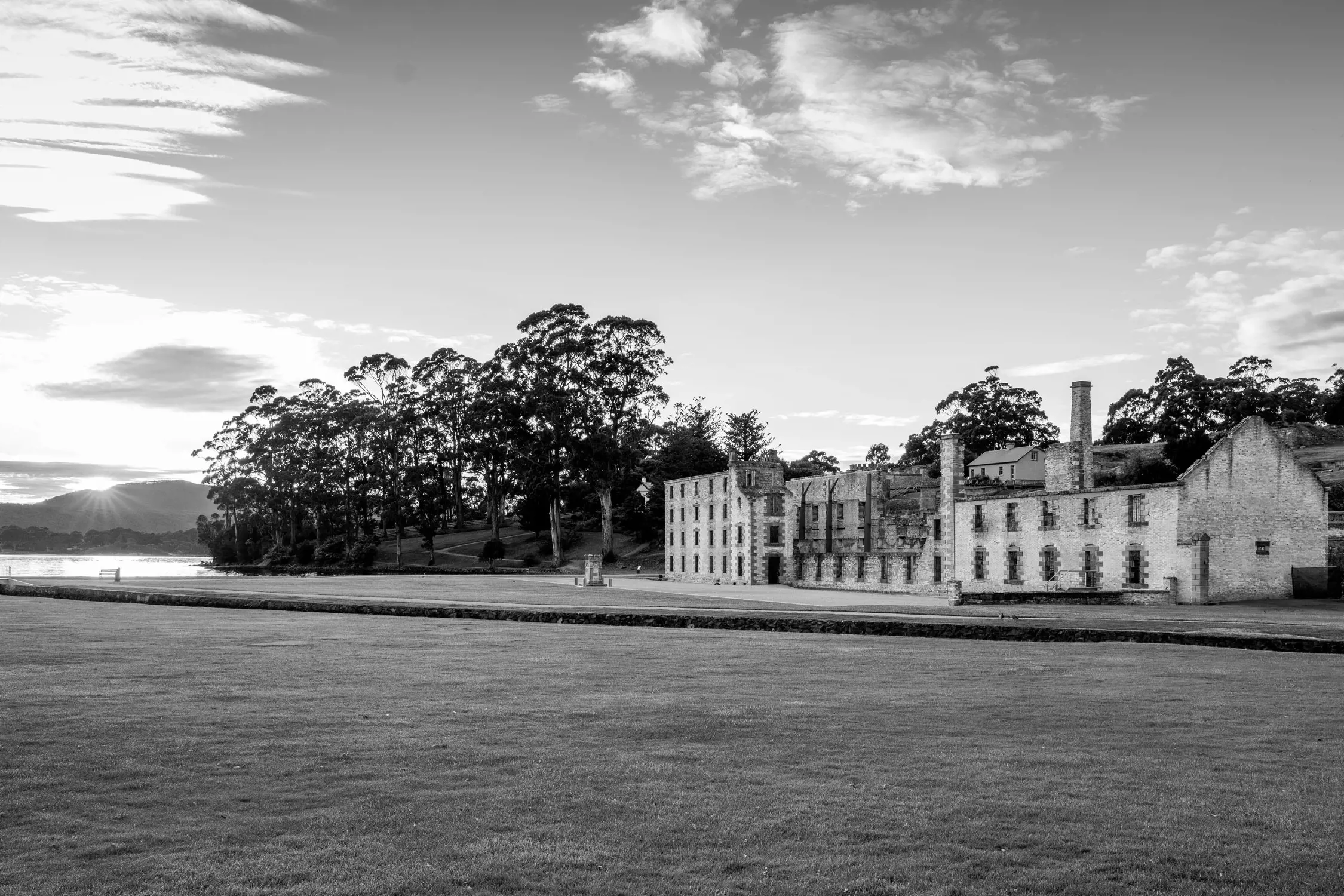 A wide lawn with the ruins of a large stone building in the background during sunset or sunrise.