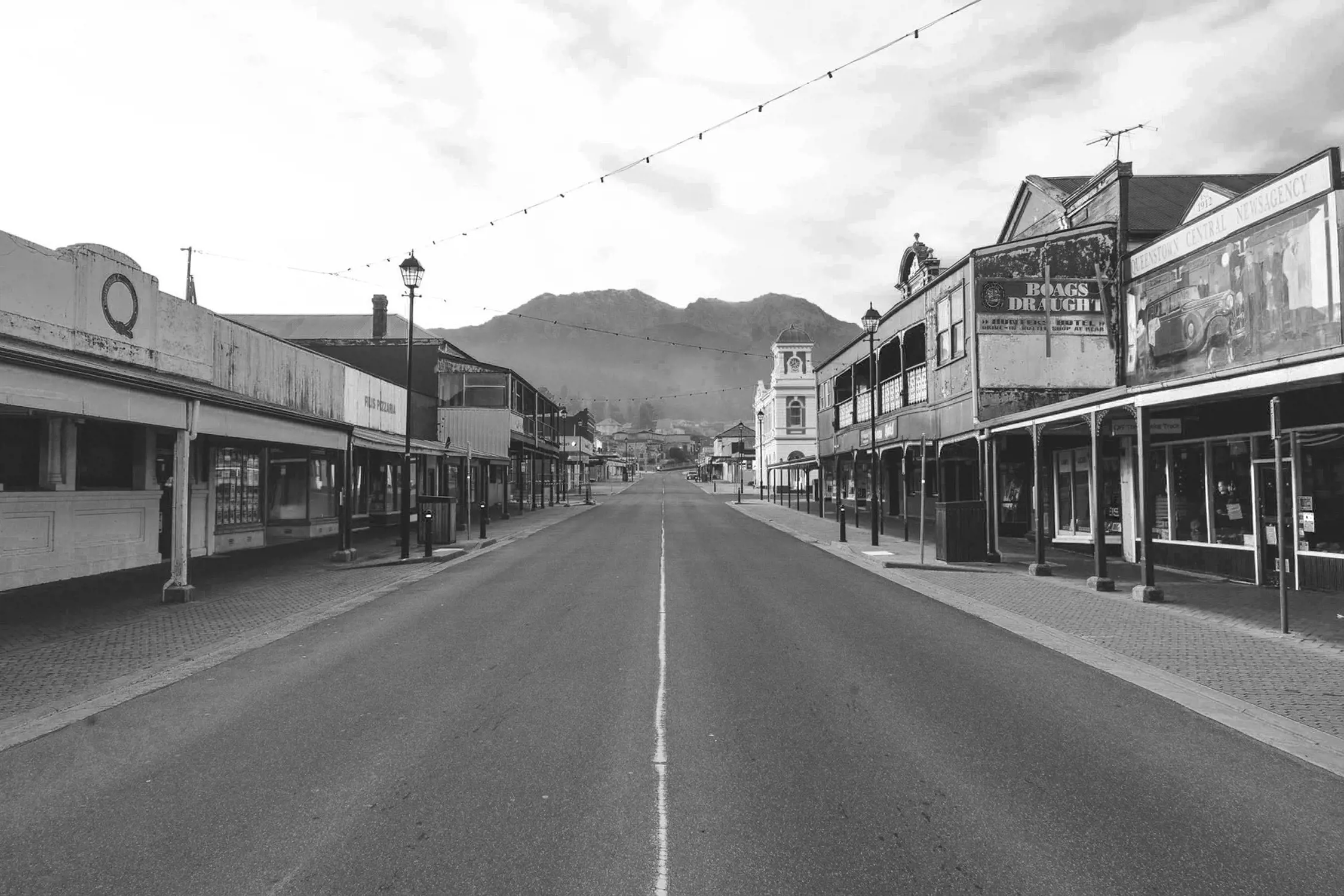 An empty main street of a town with old buildings lining both sides and mountains in the distance.