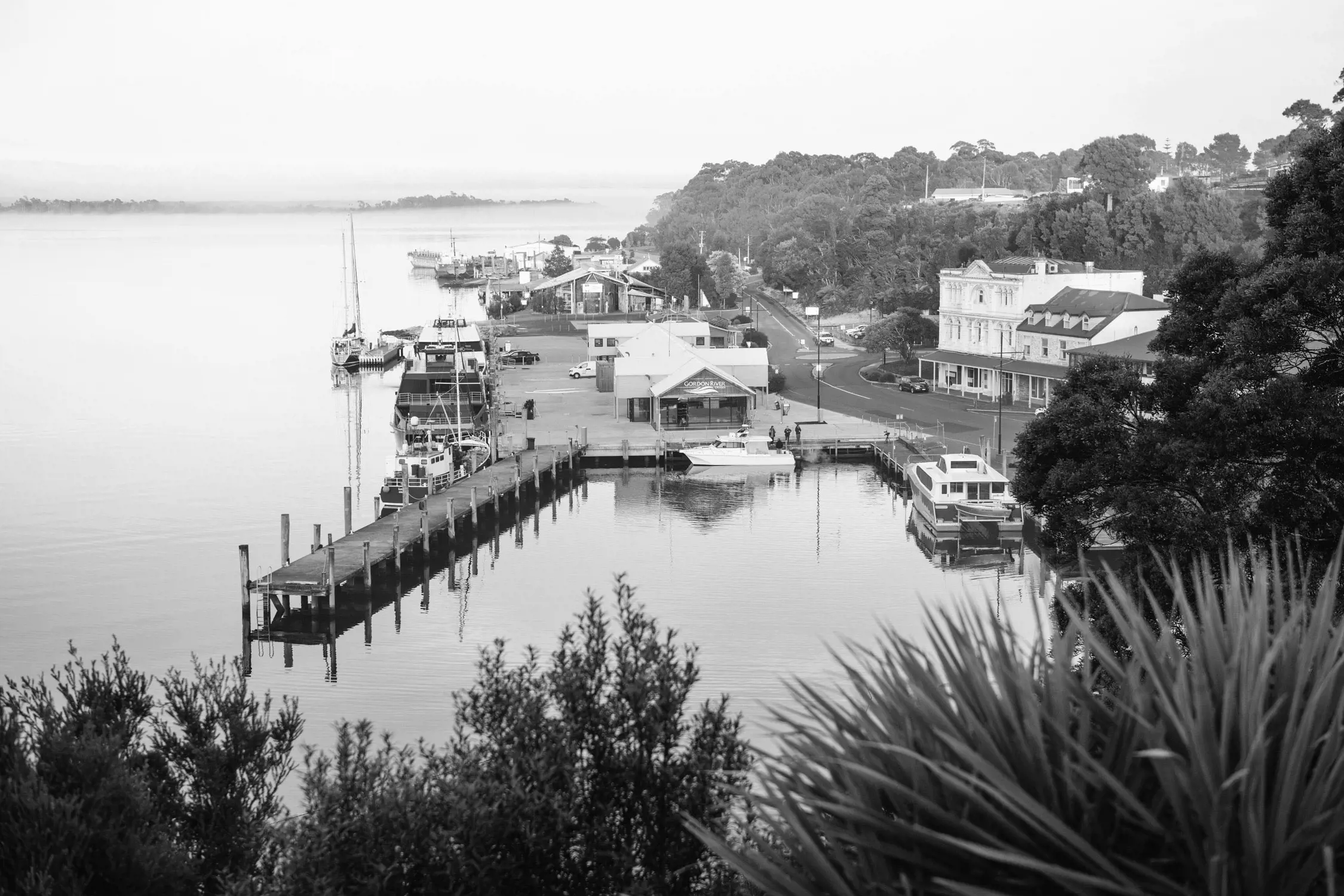 A panoramic twilight view of a coastal town harbor with boats and lights along the shoreline.