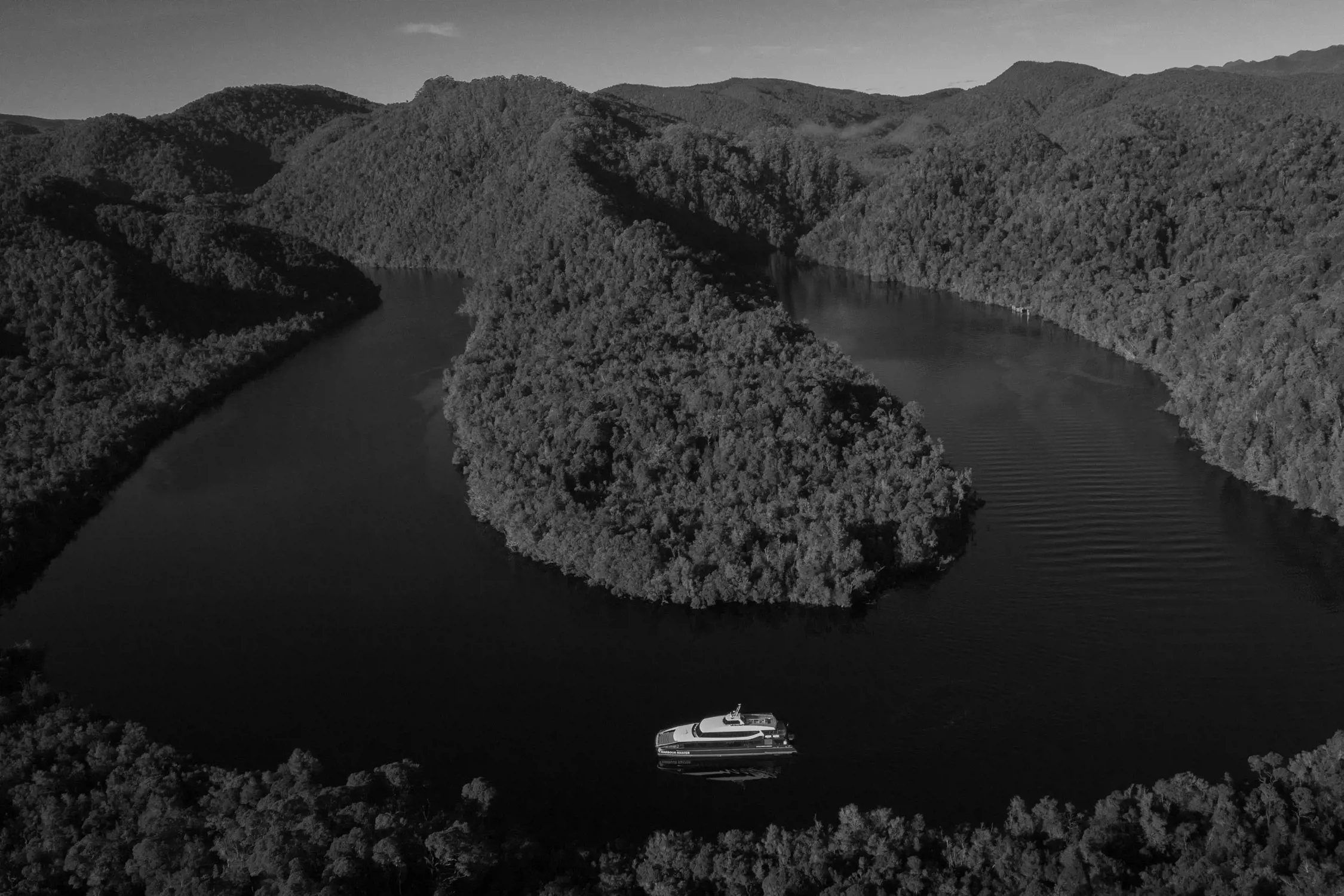A small boat sailing on a river winding through a densely forested landscape captured from above.