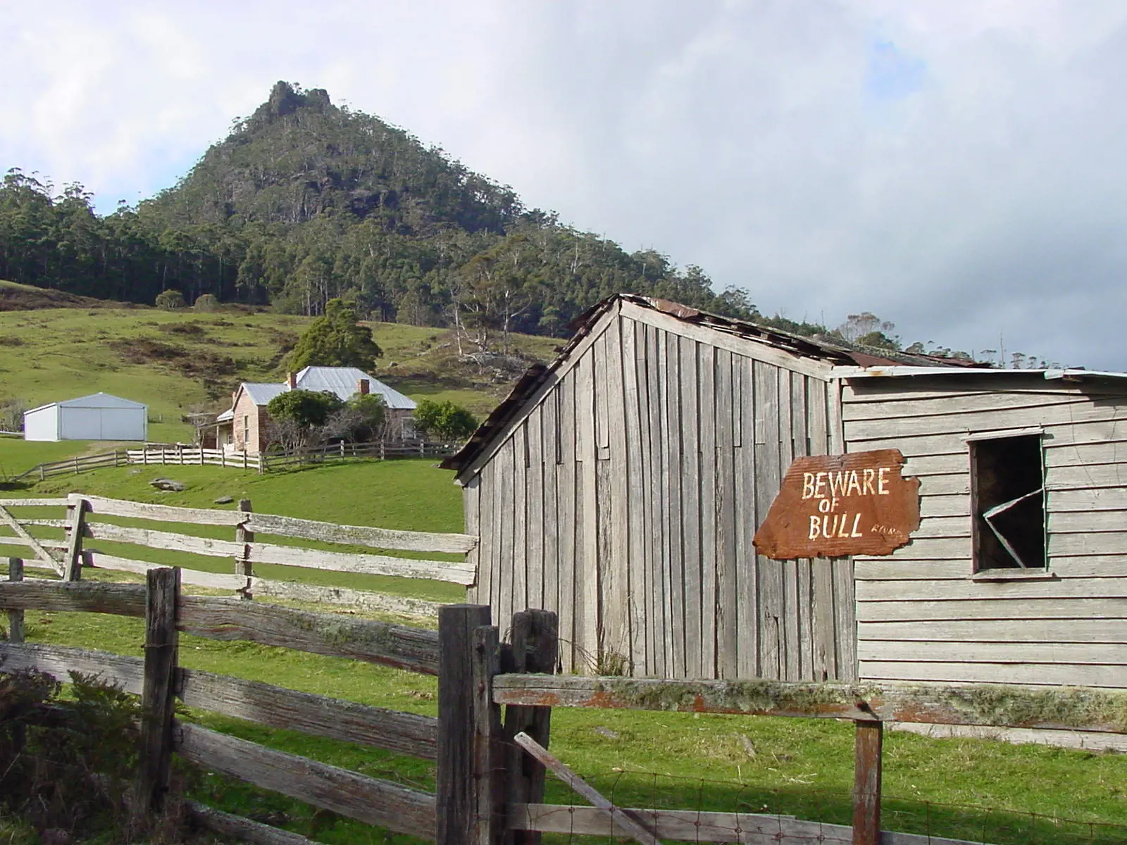 Close up image of St Marys Farm. The trees on the hill in the background and a sign on the farm door that reads 'beware of bull'.