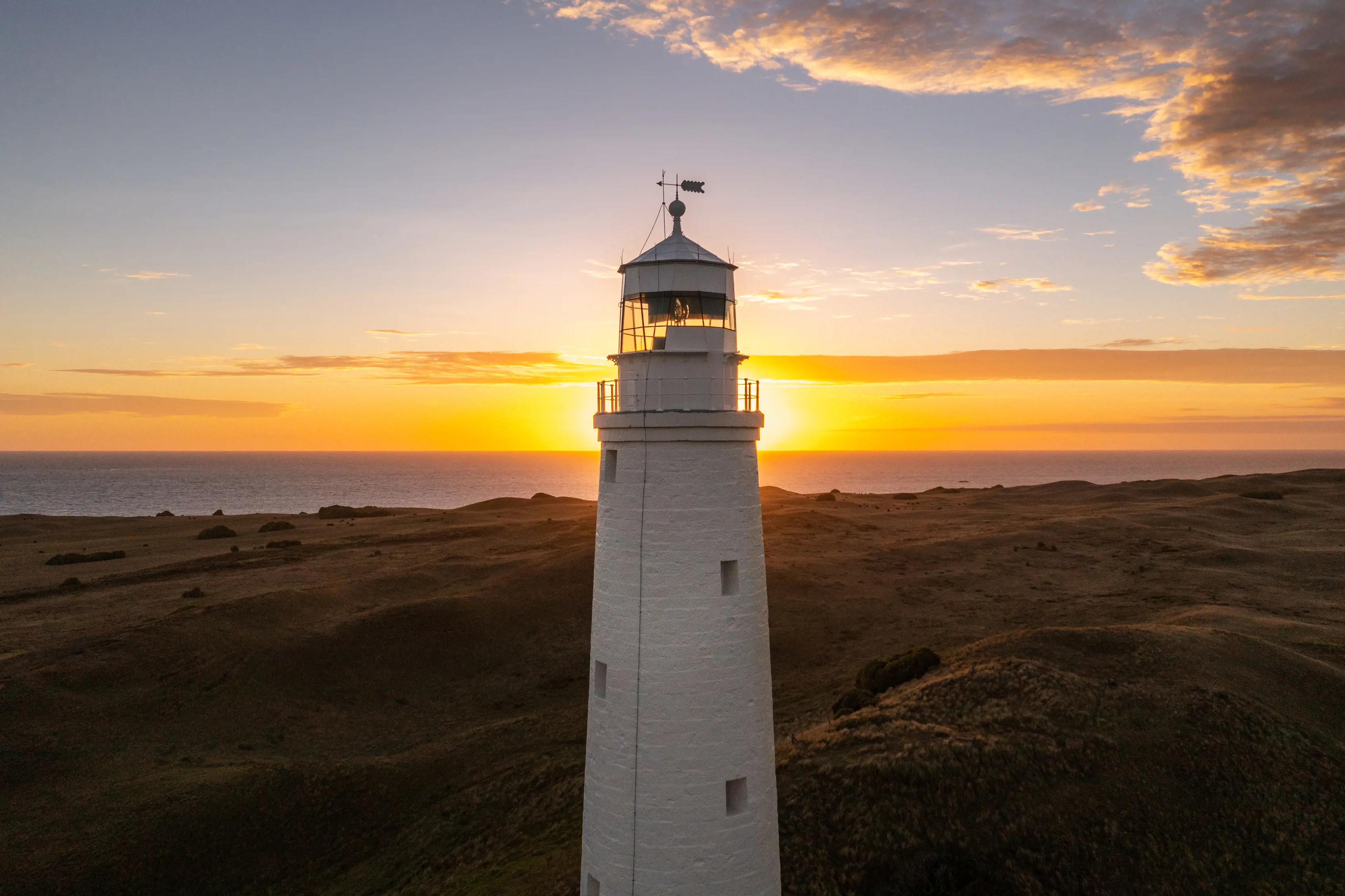 Cape Wickham Lighthouse surrounded by a sun setting horizon.