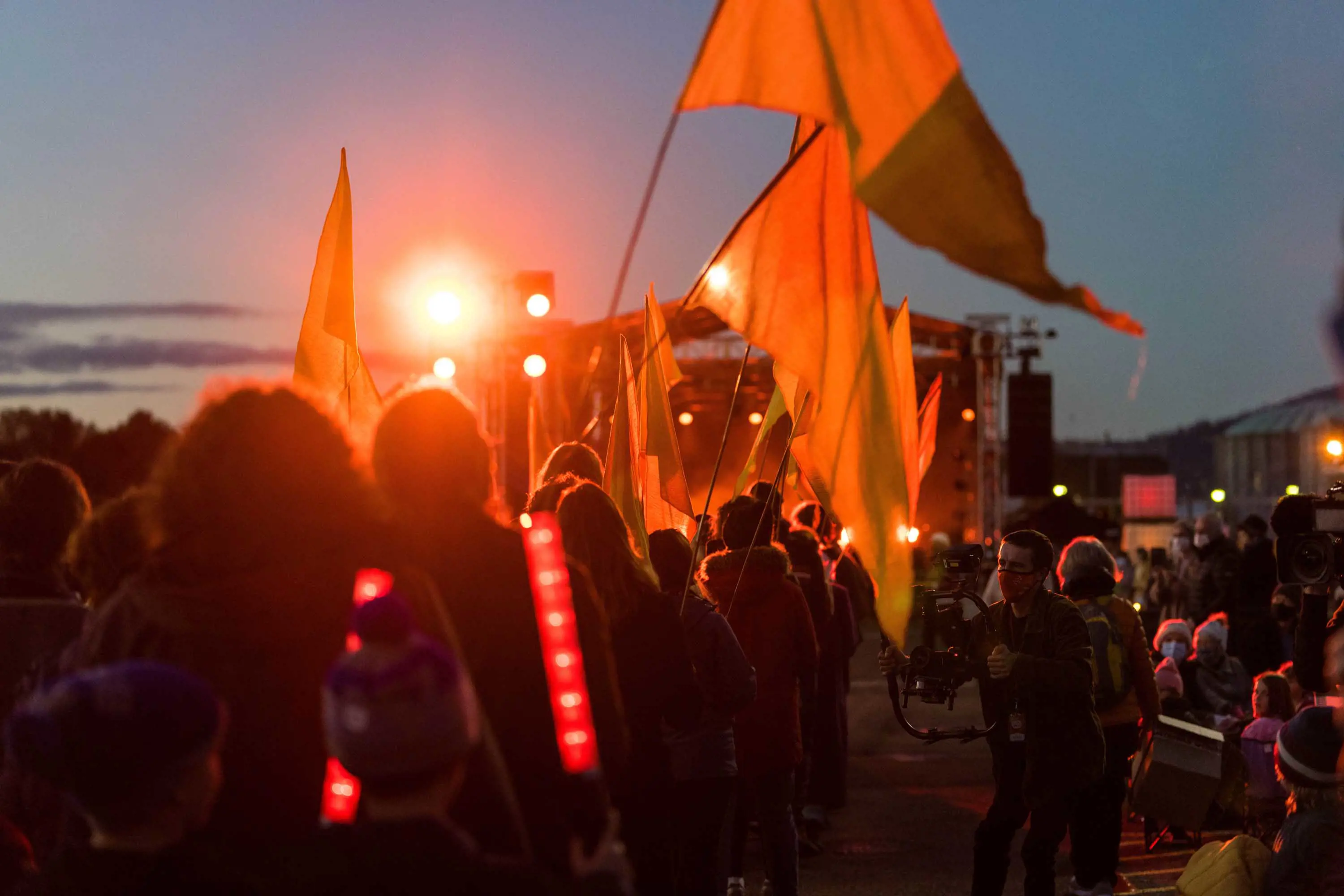 A large group of people wave flags and face a stage where a concert is being held.