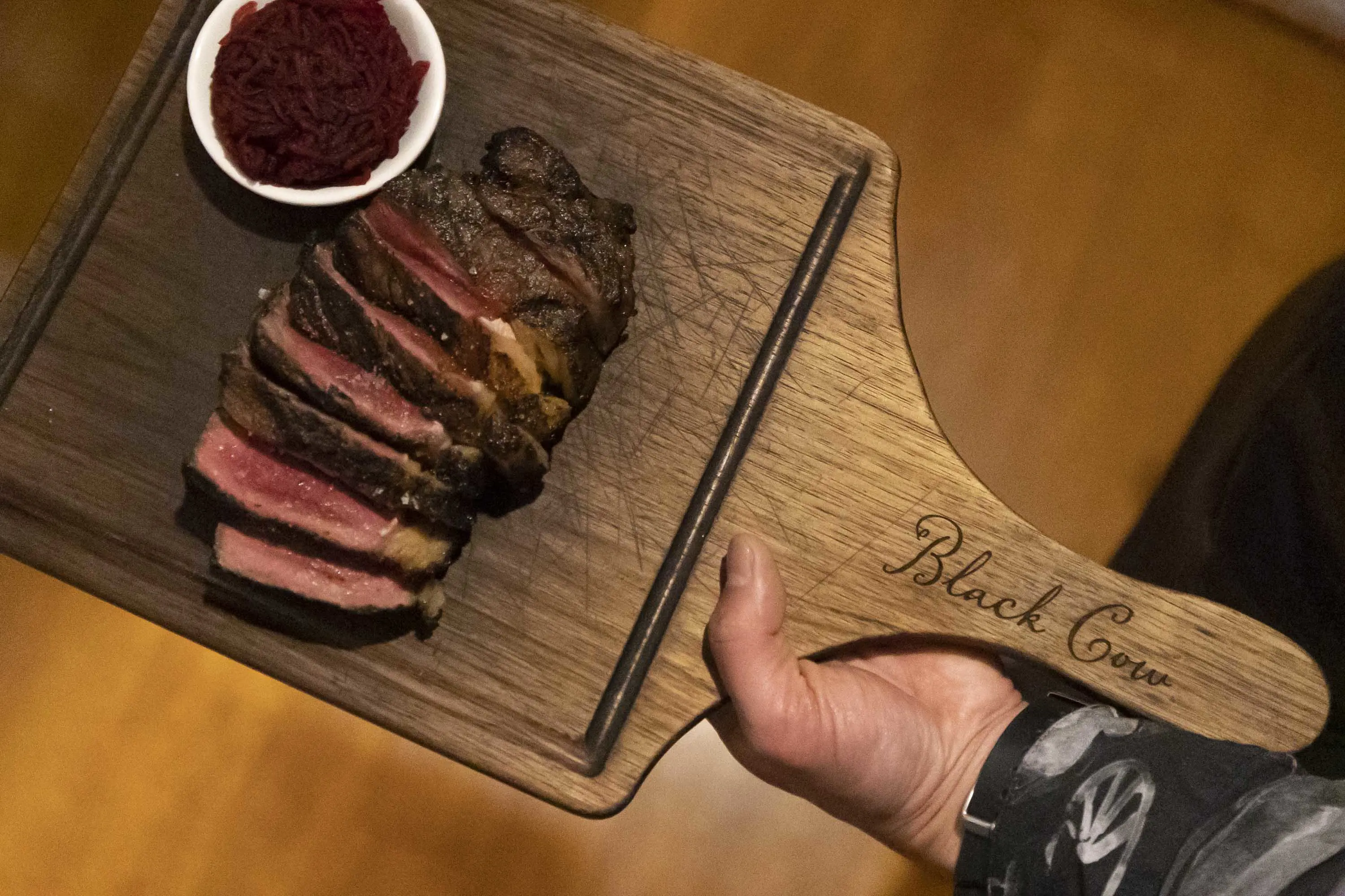 A waiter holds a wooden board with beef, cooked medium-rare and thinly sliced.