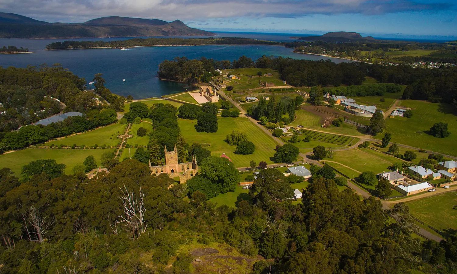 An aerial view of Port Arthur Historic Site, crisscrossed with sandstone buildings, paths through green grass and surrounded by deep green bush.