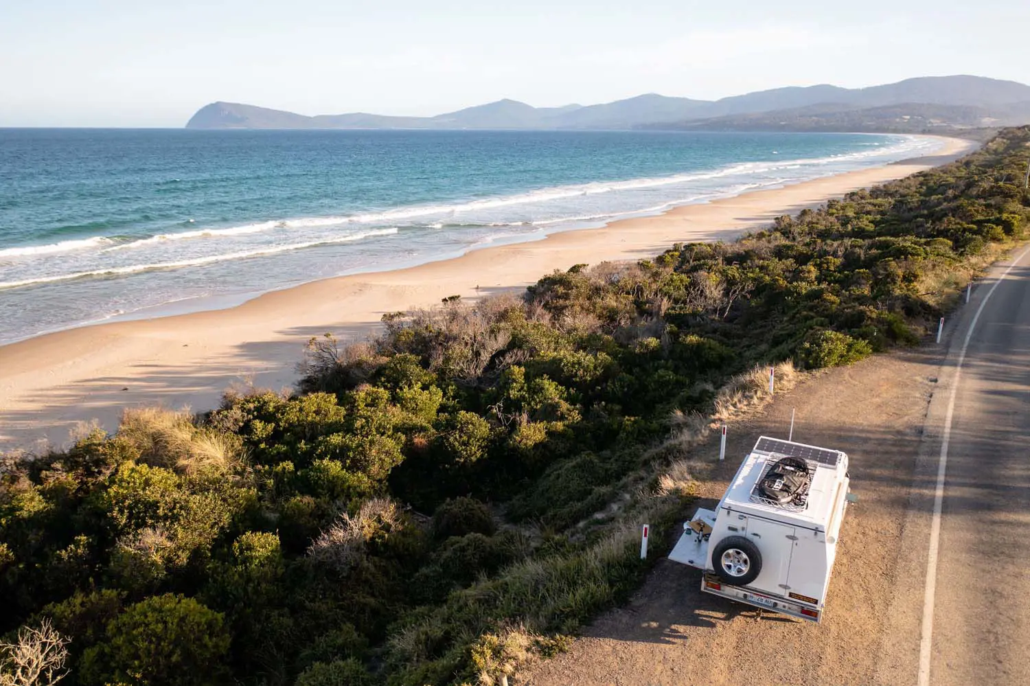 Spectacular aerial image of a caravan parked on the side of the road, next to a beach at Bicheno, on a clear sunny day.